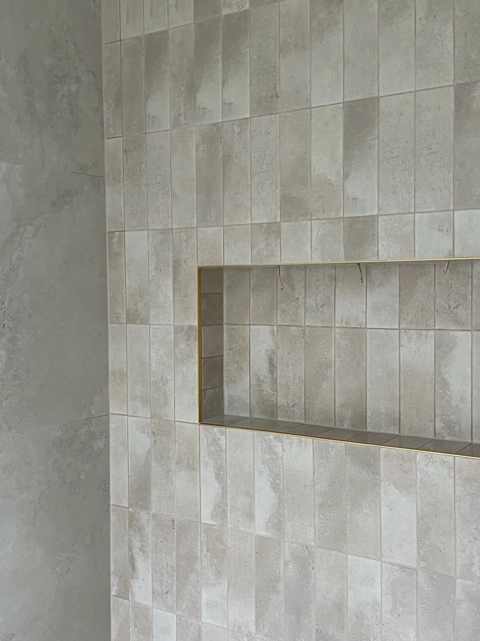 Tiled shower wall with built-in niche for toiletries, featuring a small ledge and a gold-colored trim.