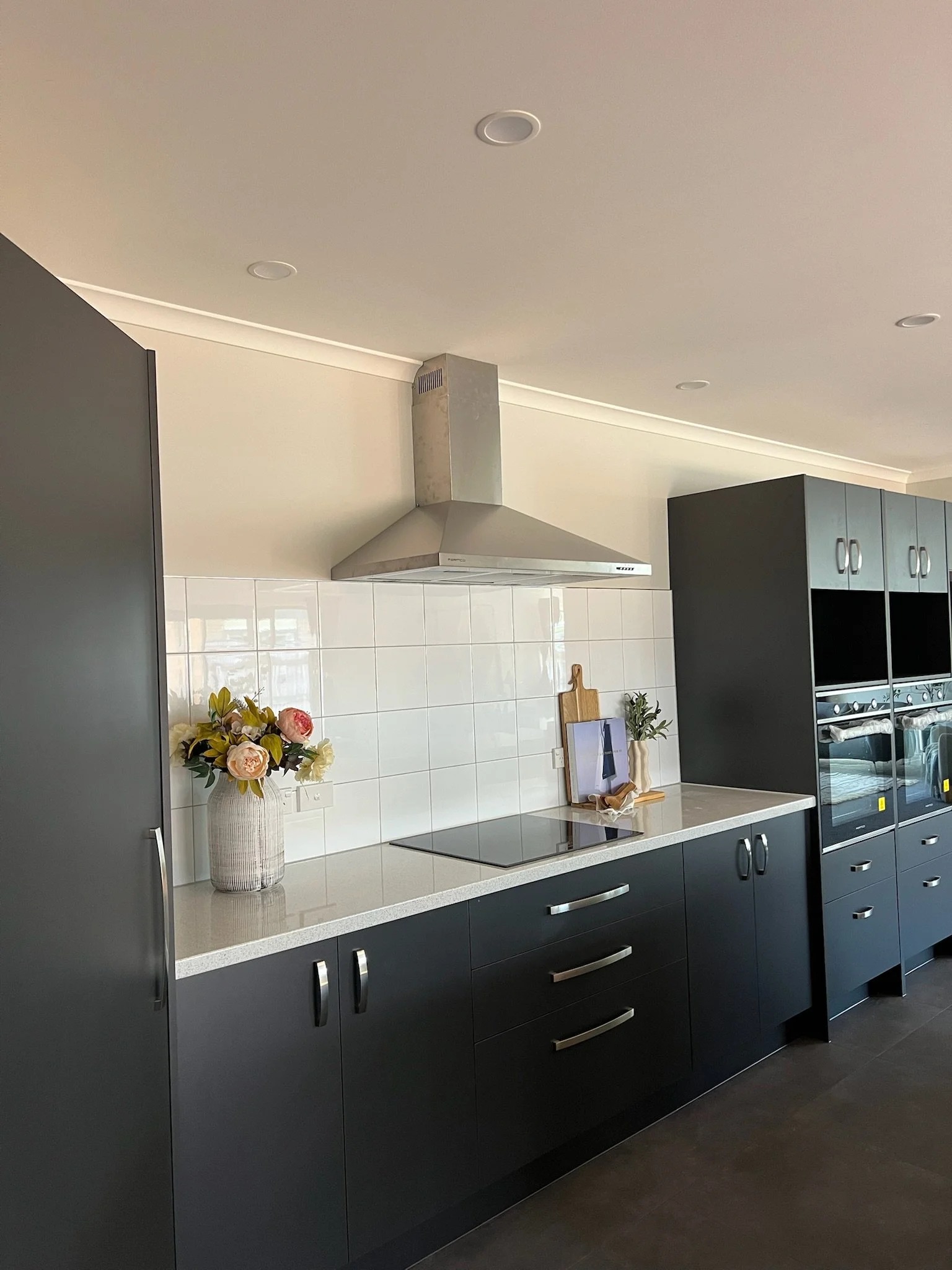 Modern kitchen with black cabinets, white countertop, stainless steel range hood, white tile backsplash.