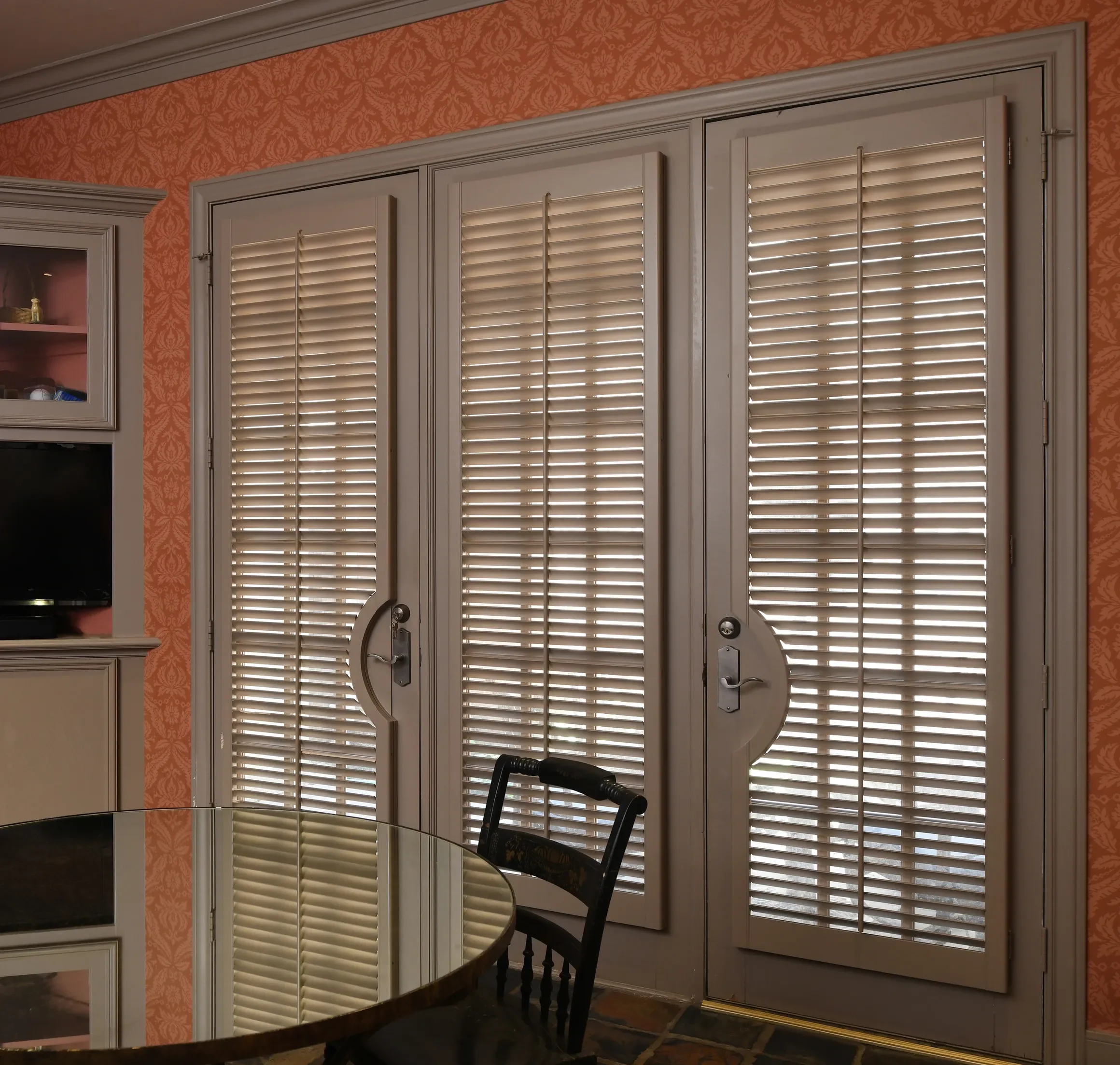 A room with beige walls, custom painted plantation shutters on windows and doors with rounded door cut-out.  2 1/2" louvers with front tilt rods, divider rails on windows, painted to match wood trim, chrome hinges.