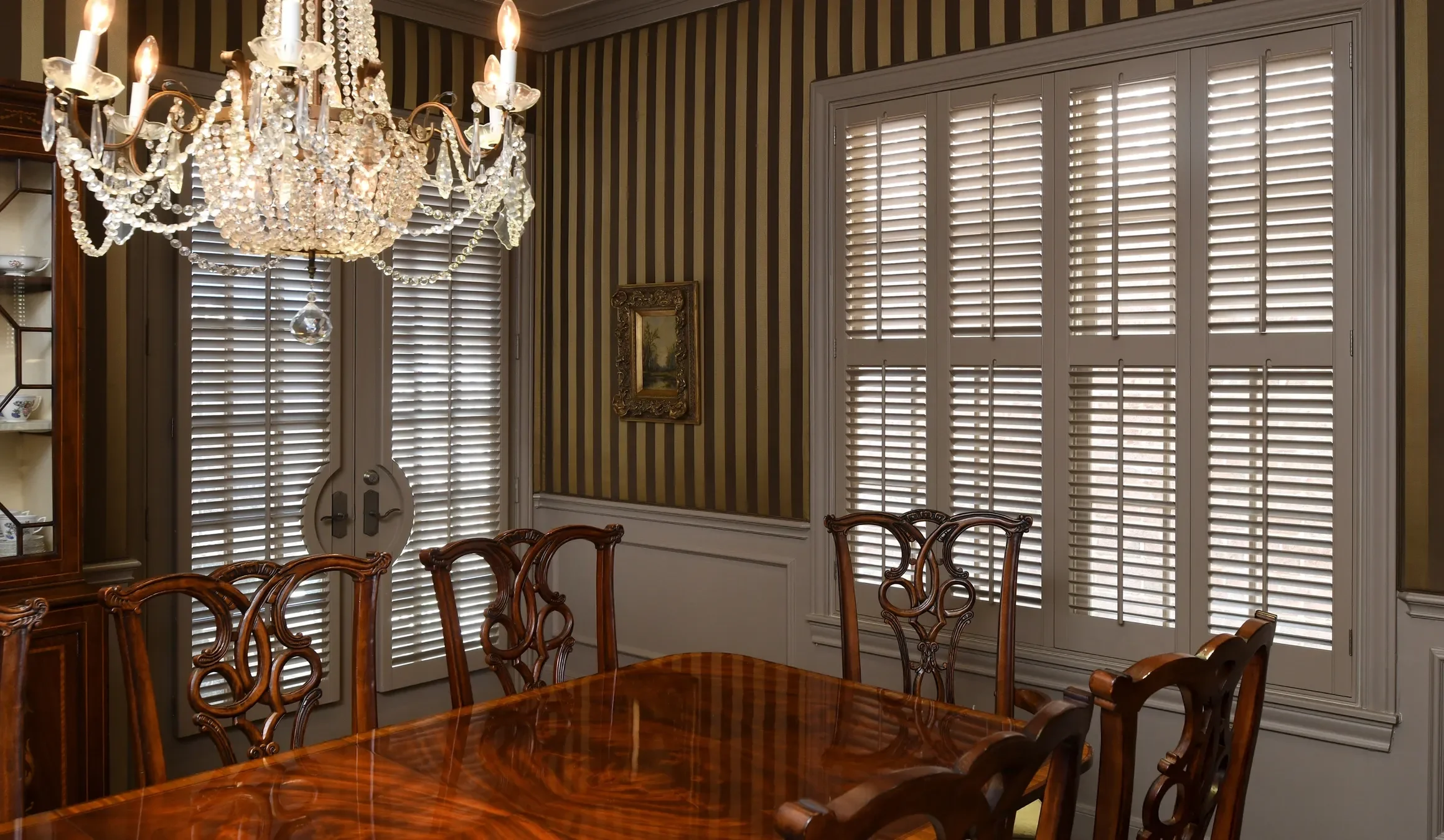 A room with beige walls, custom painted plantation shutters on windows and doors with rounded door cut-out.  2 1/2" louvers with front tilt rods, divider rails on windows, painted to match wood trim, chrome hinges.