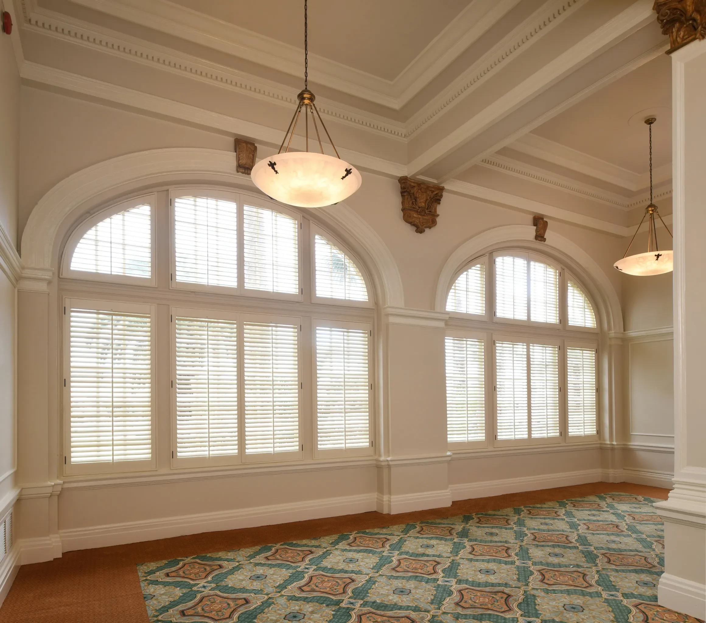 An elegant room with large arched windows with custom white wood shutters with traditional front tilt rods, arch top shutters.