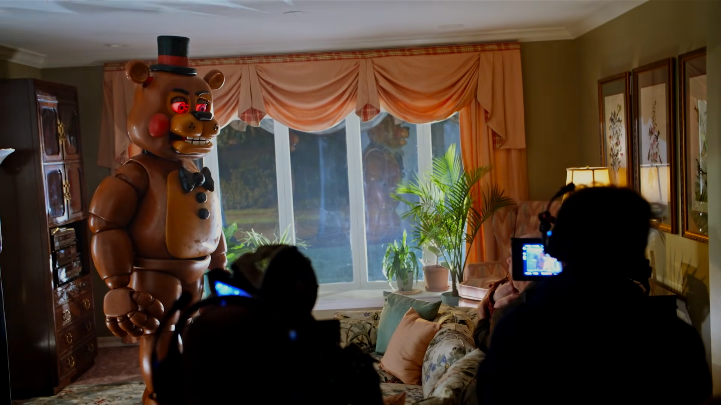 A person filming a person in a bear costume with glowing red eyes in a living room.
