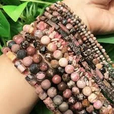 Multiple strands of beaded jewelry featuring pink, black, and multicolored round beads being held on a person's arm.
