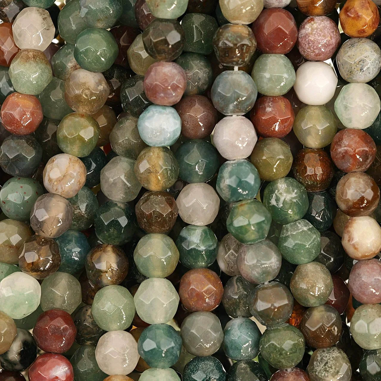 Close-up of a collection of small, round, colorful beads, some with a faceted surface, in shades of green, brown, white, red, and tan.