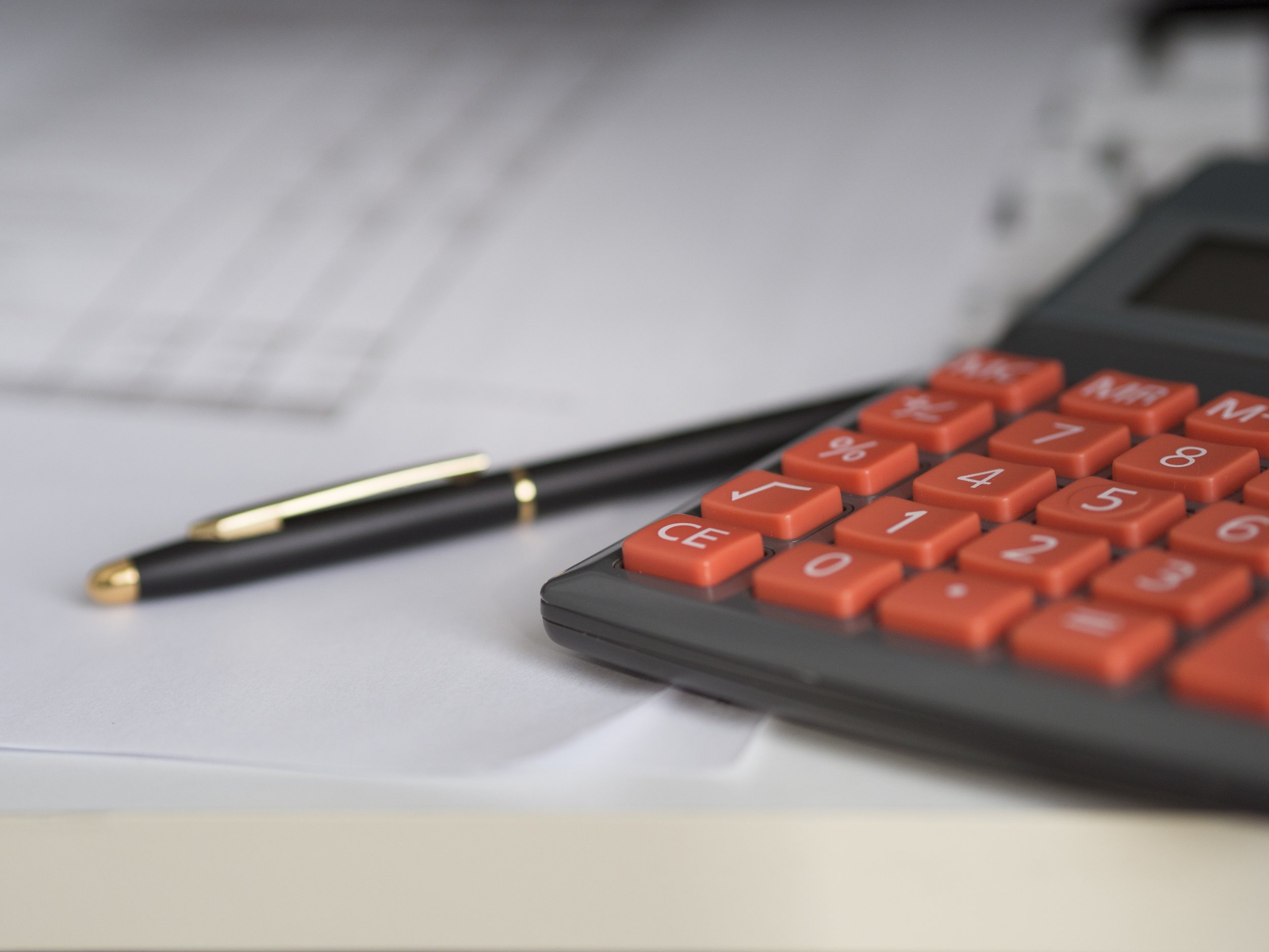 Close-up of an orange calculator, a black pen with gold accents, and some papers on a white desk.