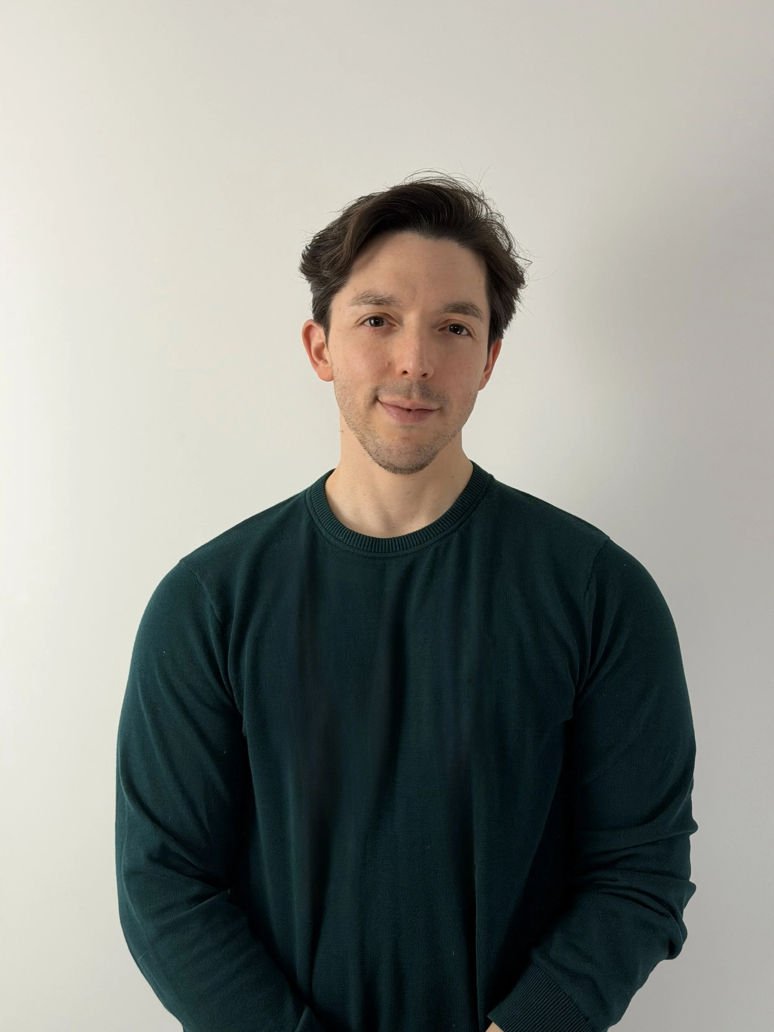 A young Canadian accountant with dark, styled hair and slight facial hair, wearing a dark green long-sleeve shirt, standing against a plain white background.