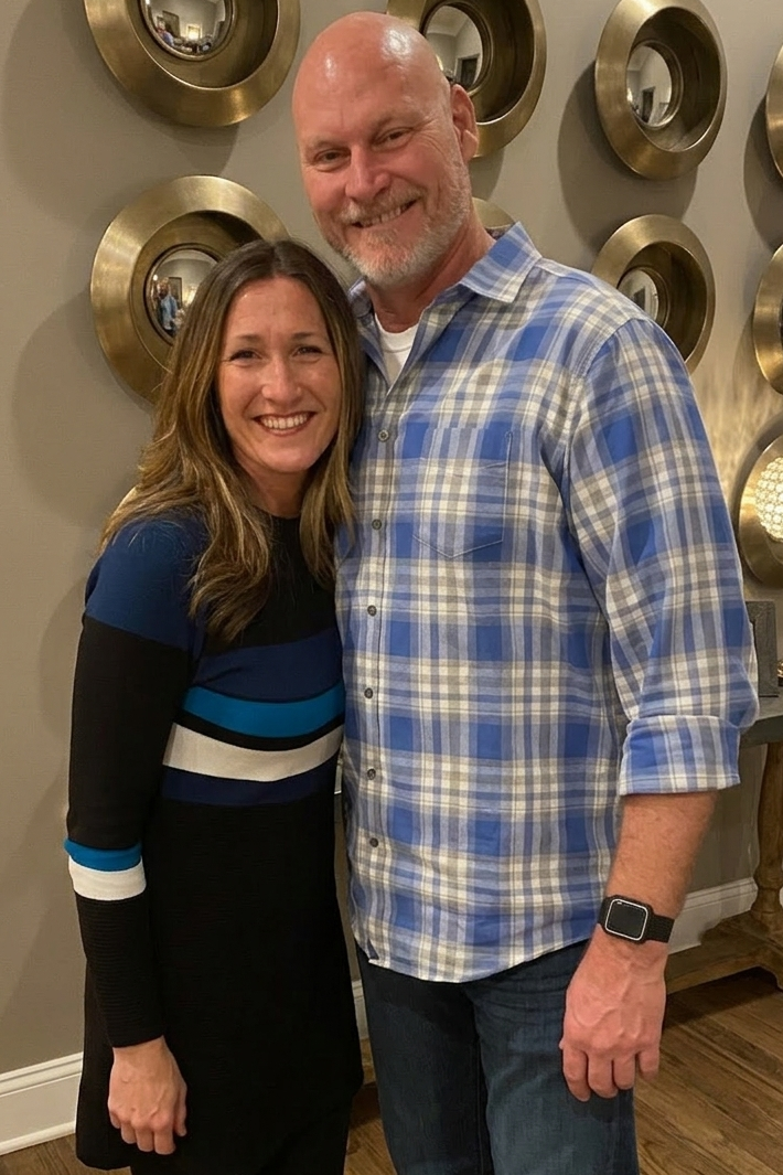 A smiling woman and man standing together indoors, with decorative round mirrors on the wall behind them.