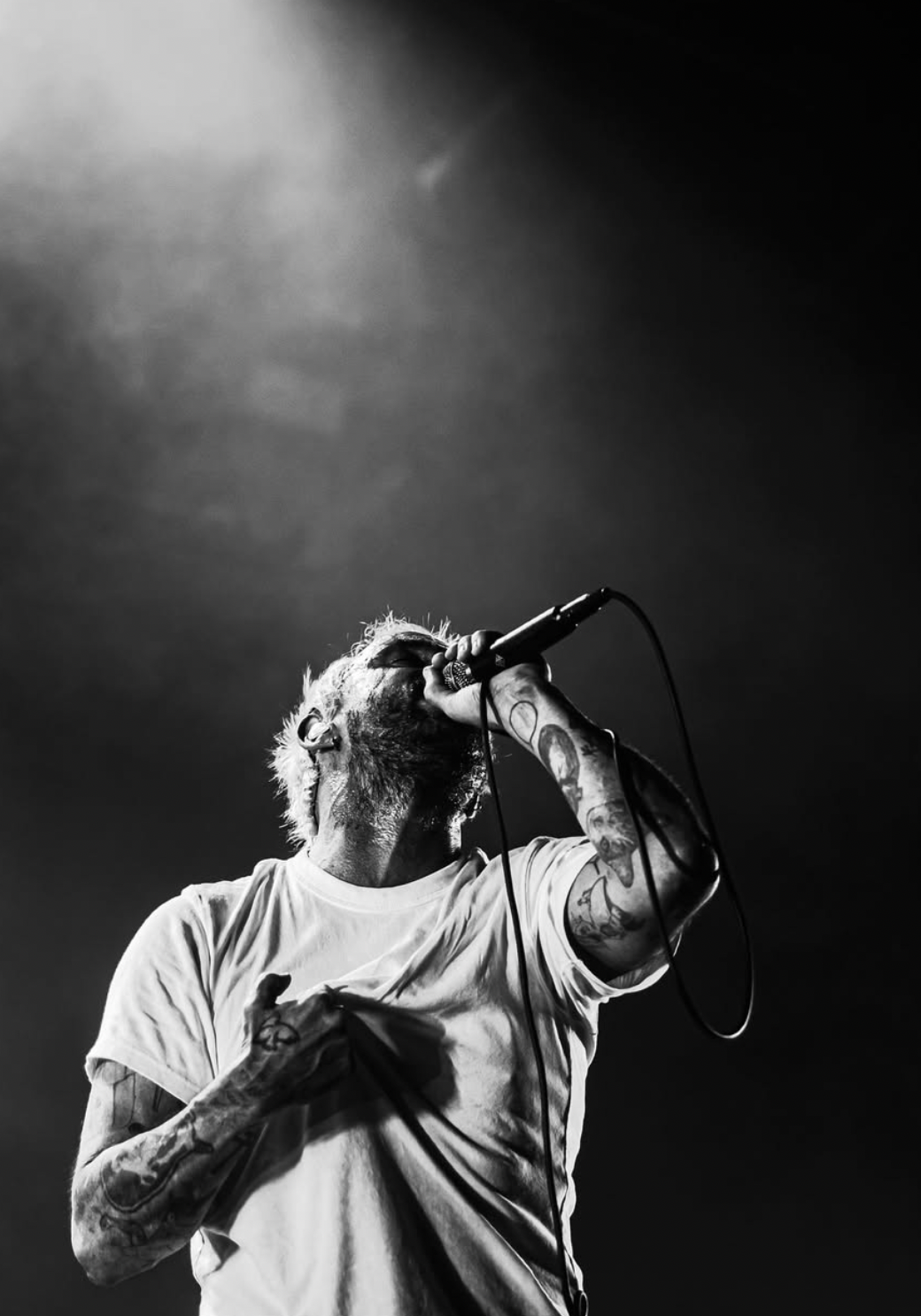A black and white photo of a tattoos man singing passionately into a microphone on stage.