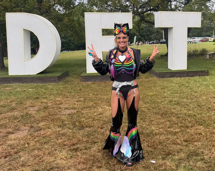 Lauren in a dark rainbow festival look at the festival sign