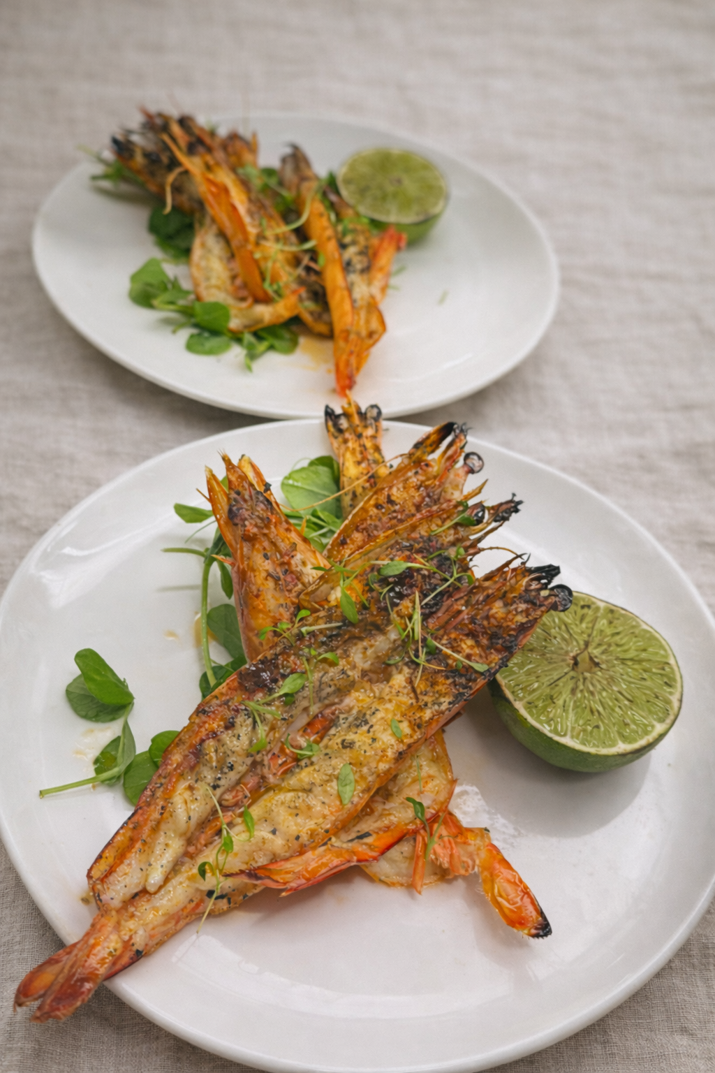 Grilled miso prawns with watercress and lime halves on white plates