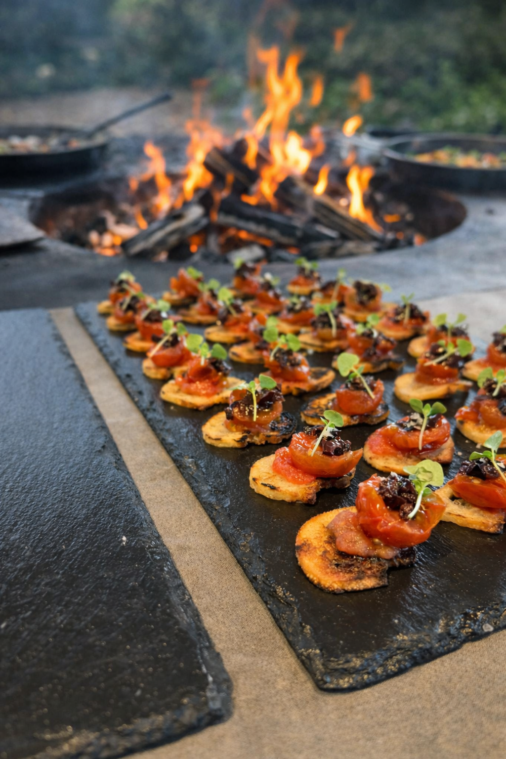 Appetizers topped with cherry tomatoes and herbs are arranged on a slate serving platter canapés | functions | Mana Kai Catering Sydney