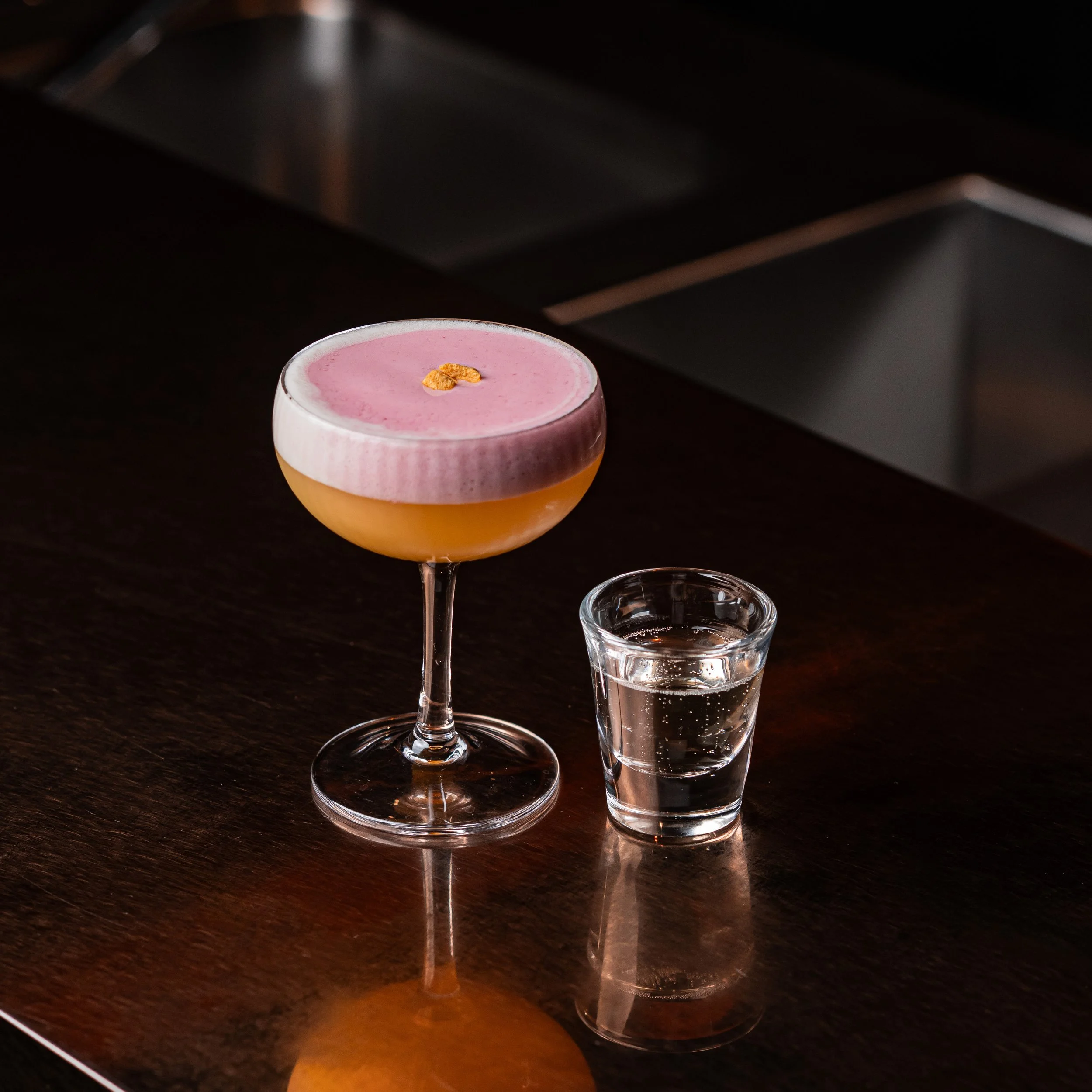 A Porn Star Martini cocktail, finished with a pink hibiscus foam on top, with passion fruit crumble, served with a shot of Prosecco.