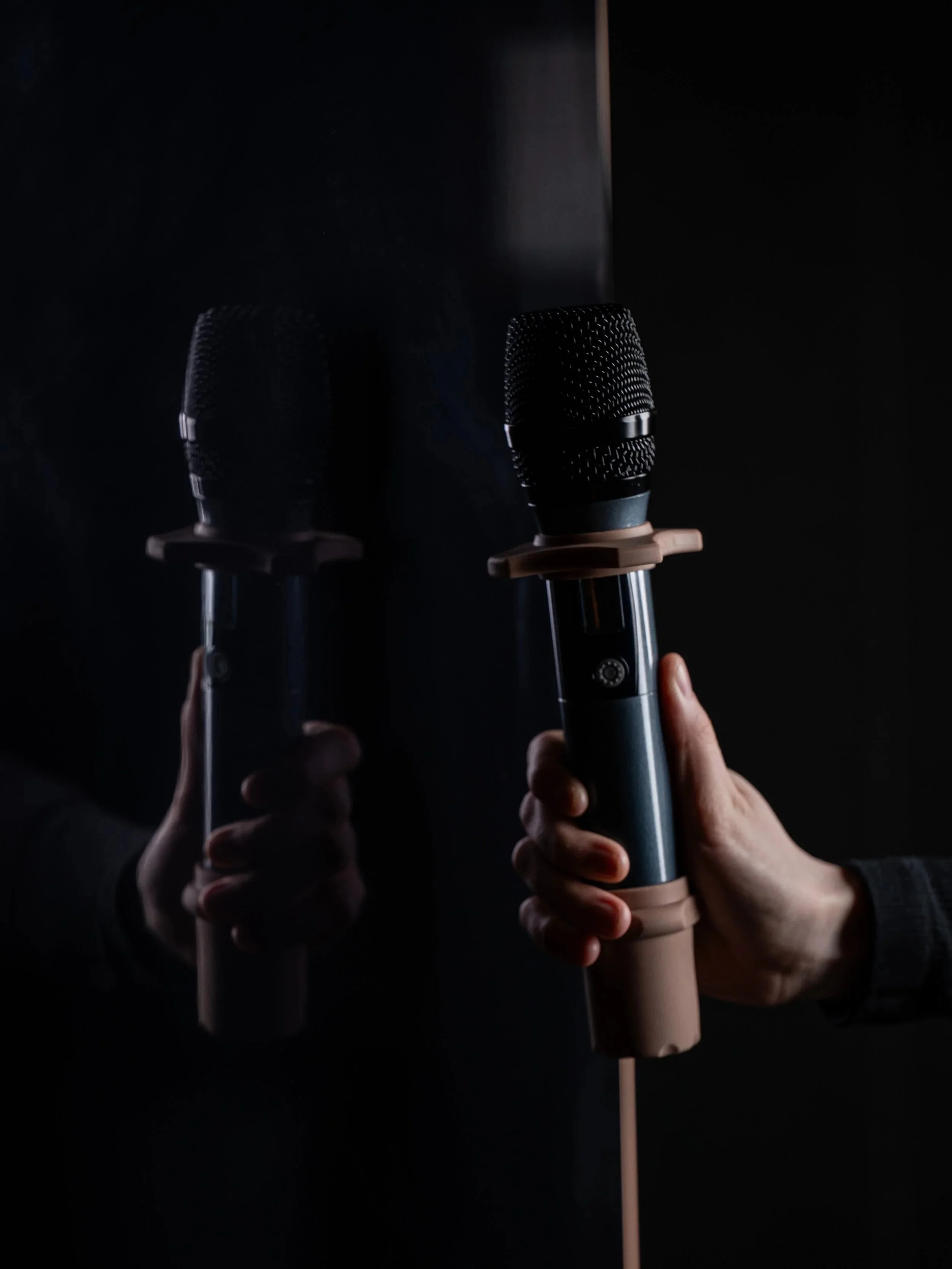 Two handheld microphones, one held by a person's hand and one reflected in a mirror, in VOX Karaoke Cocktail Bar.
