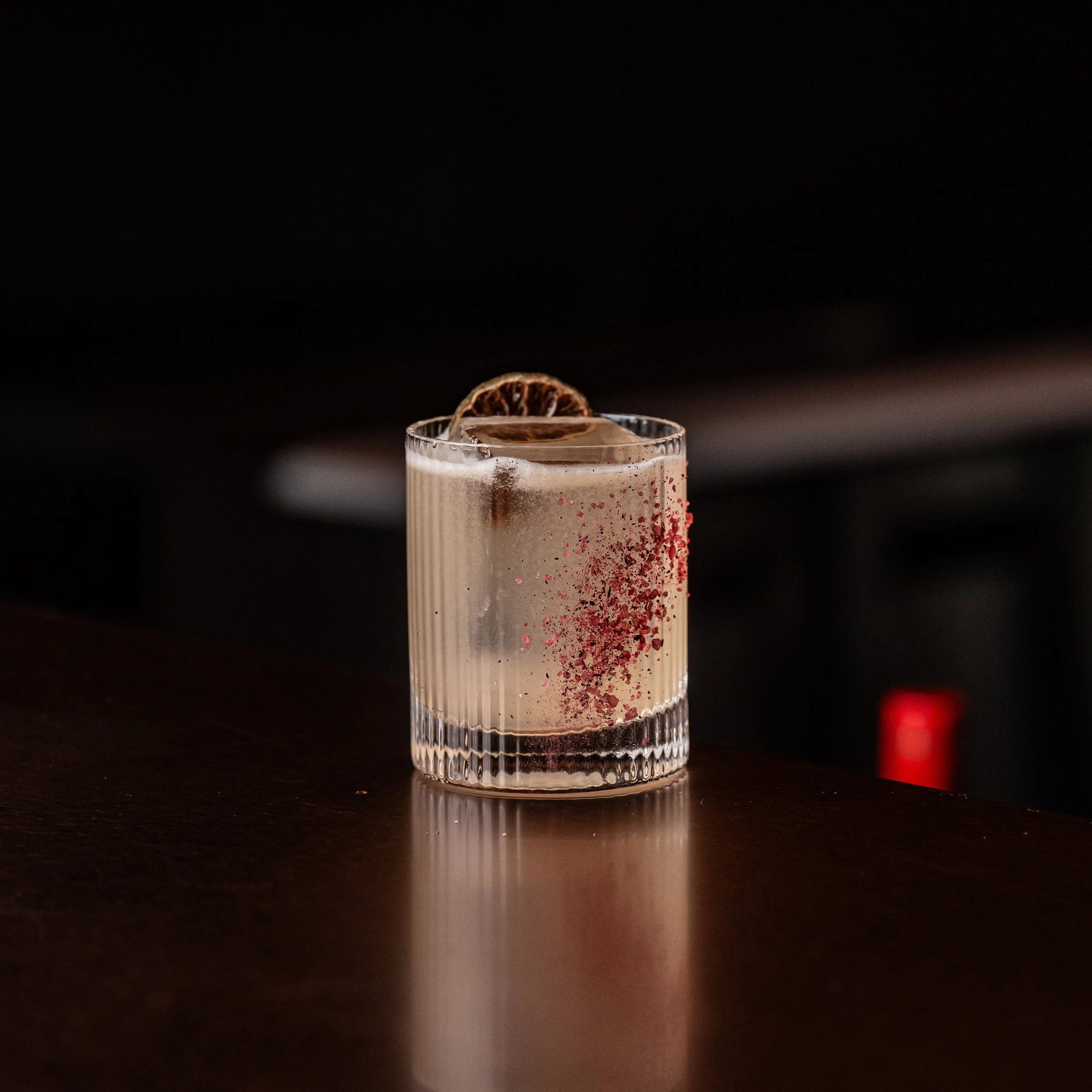 A Belle Margarita cocktail, in a clear, ribbed glass garnished with a dried lime slice, with hibiscus salt sprinkled on the glass.
