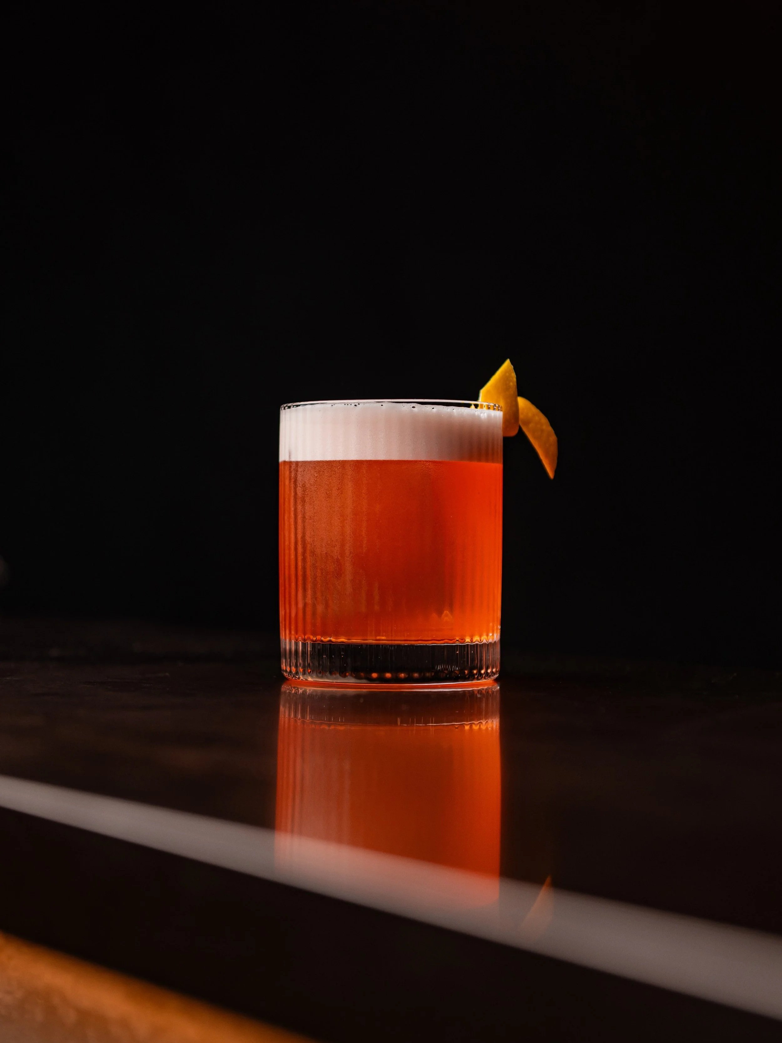 A cocktail in a hand-blown ribbed glass garnished with a lemon twist.