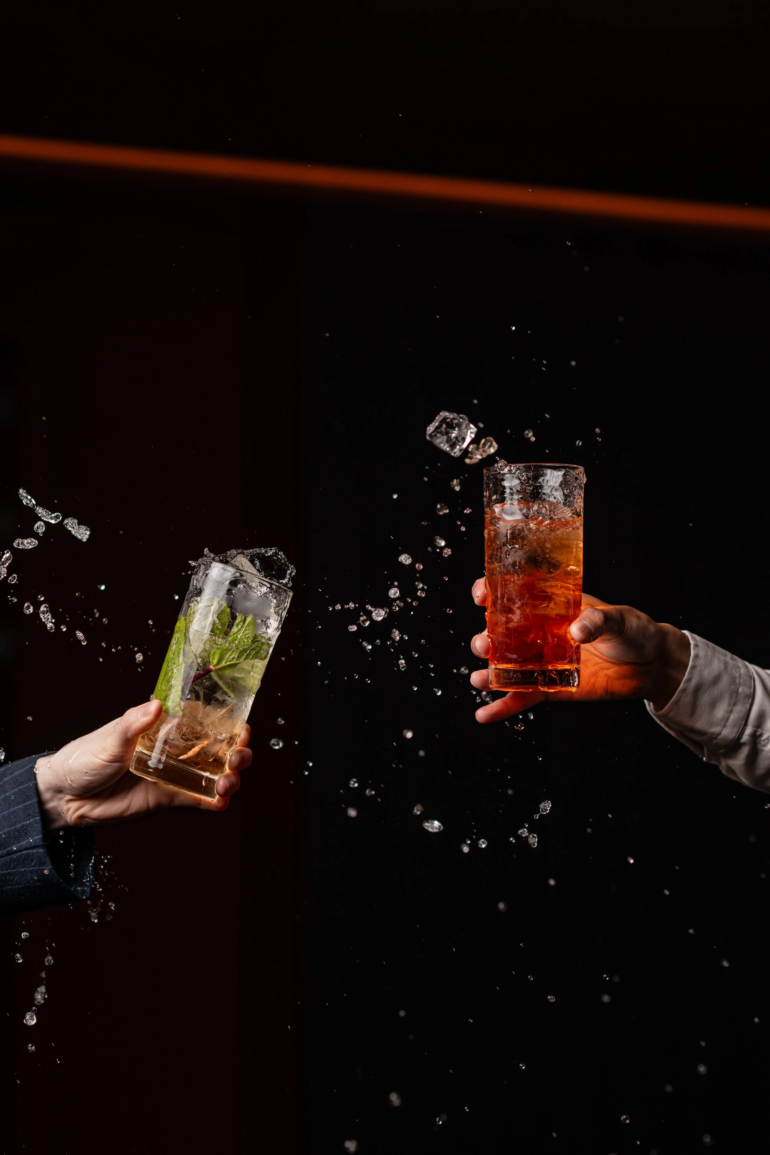 Two people holding glasses and splashing their drinks.