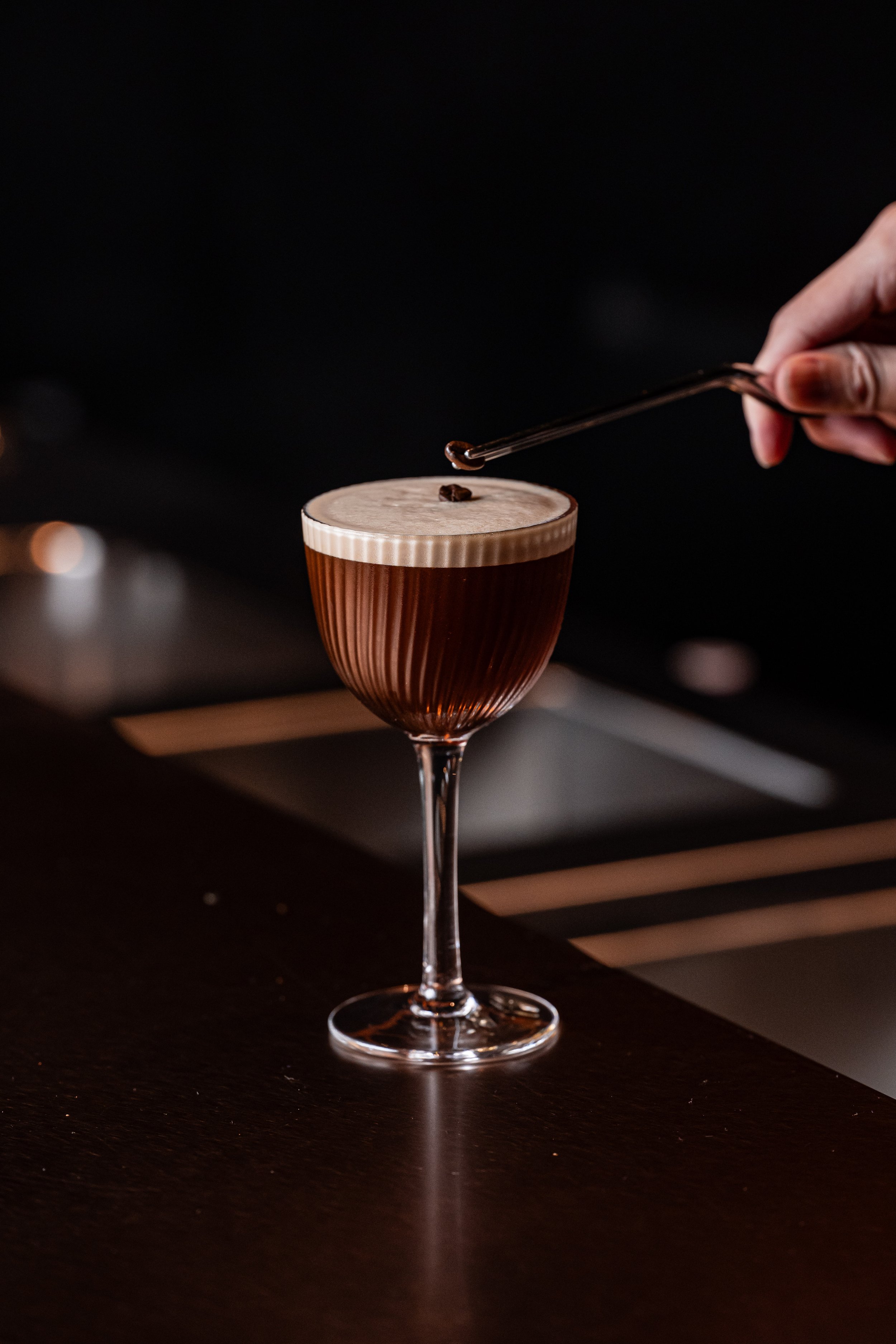 An Espresso Martini cocktail, garnished with coffee beans placed by tongs.