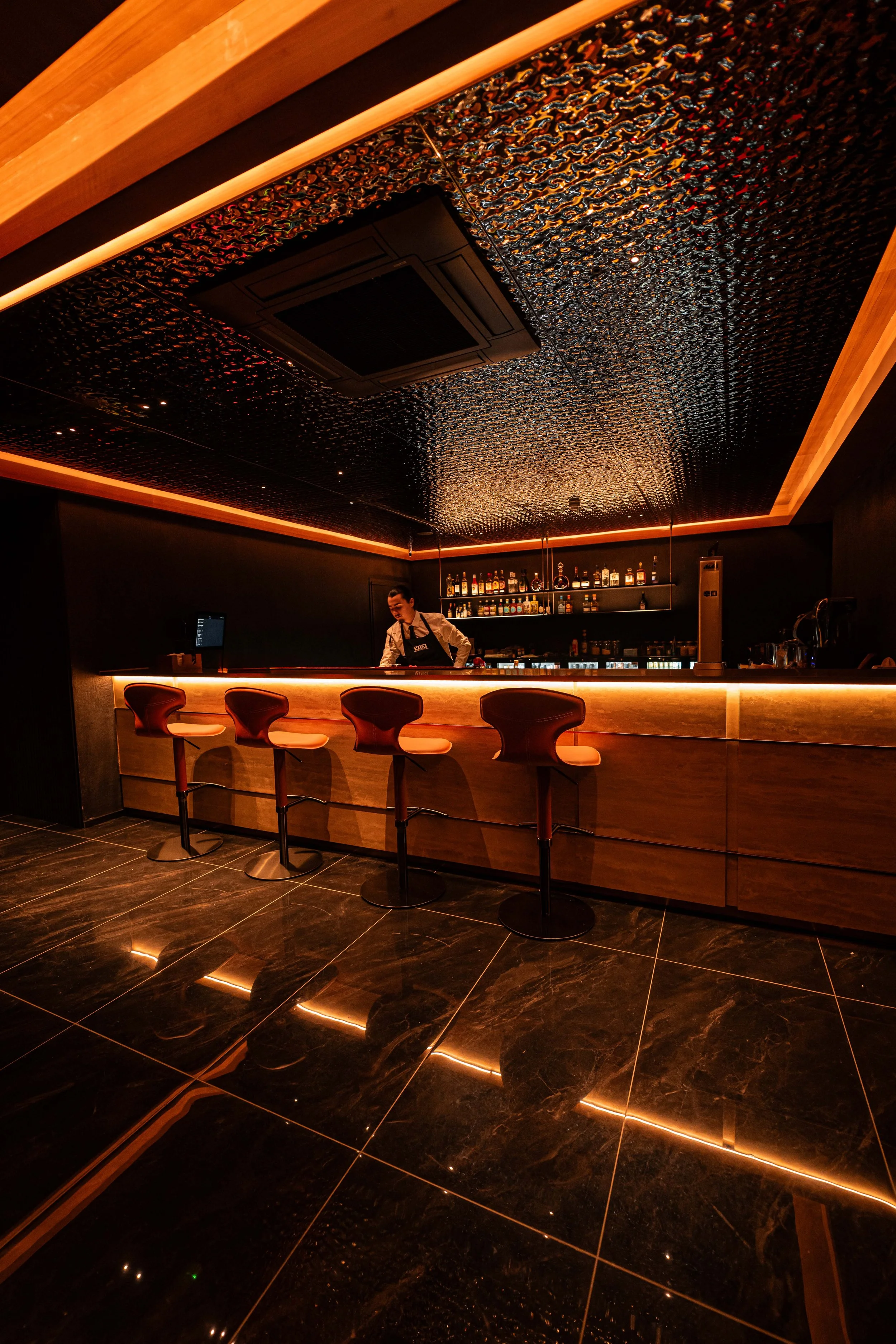 A modern bar with a dark, textured ceiling and illuminated accents.