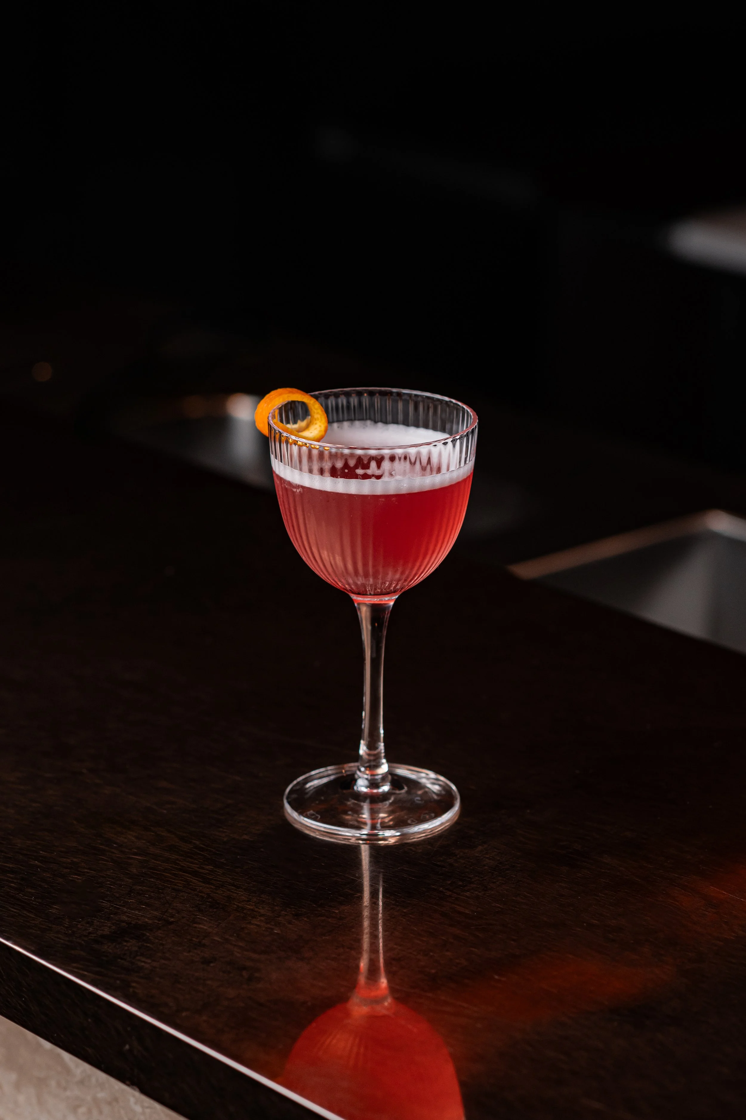 A Cosmopolitan cocktail, garnished with an orange peel twist.