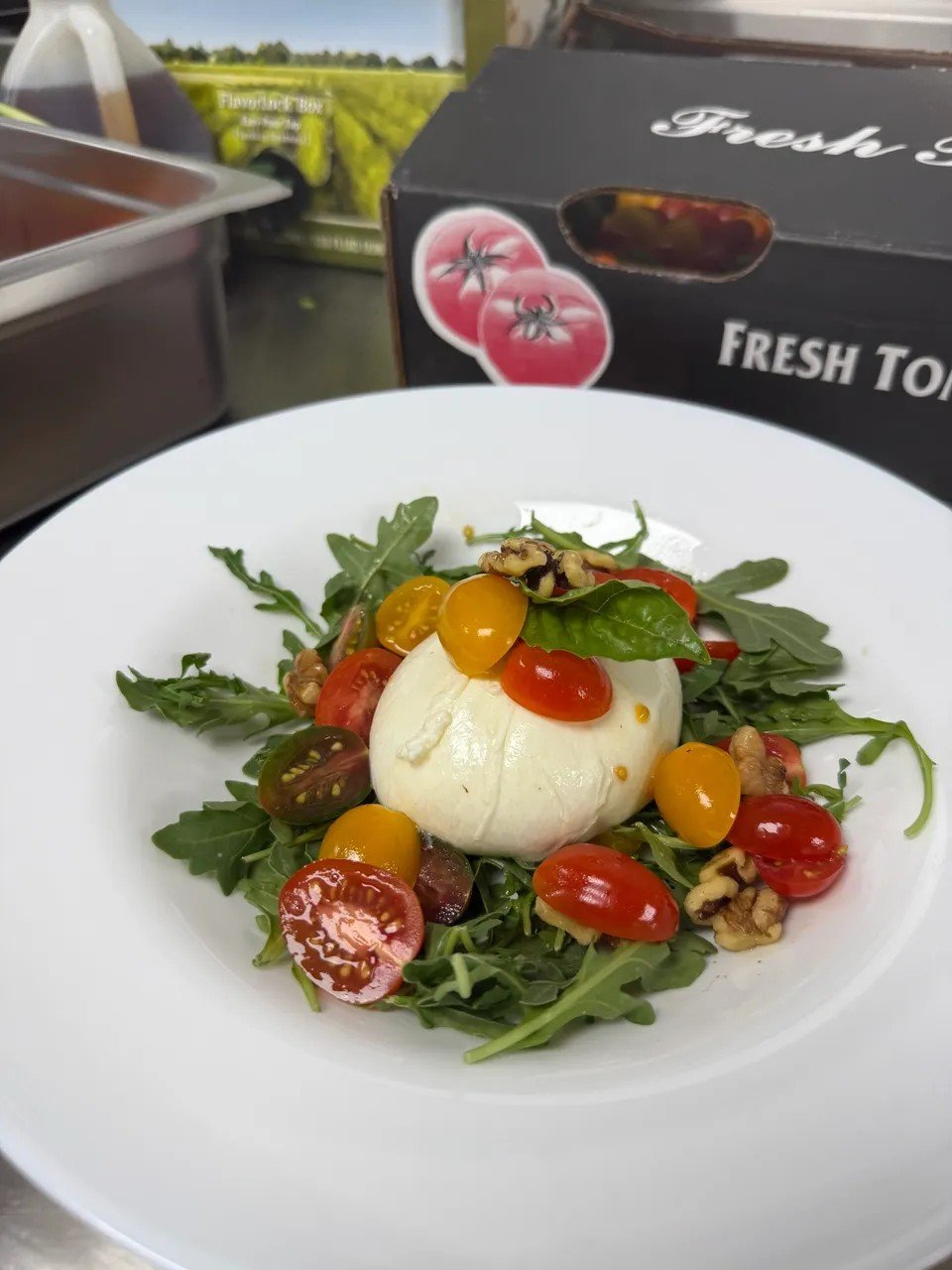 Caprese salad with cherry tomatoes, basil, walnuts, and fresh mozzarella on a bed of arugula in a white bowl.