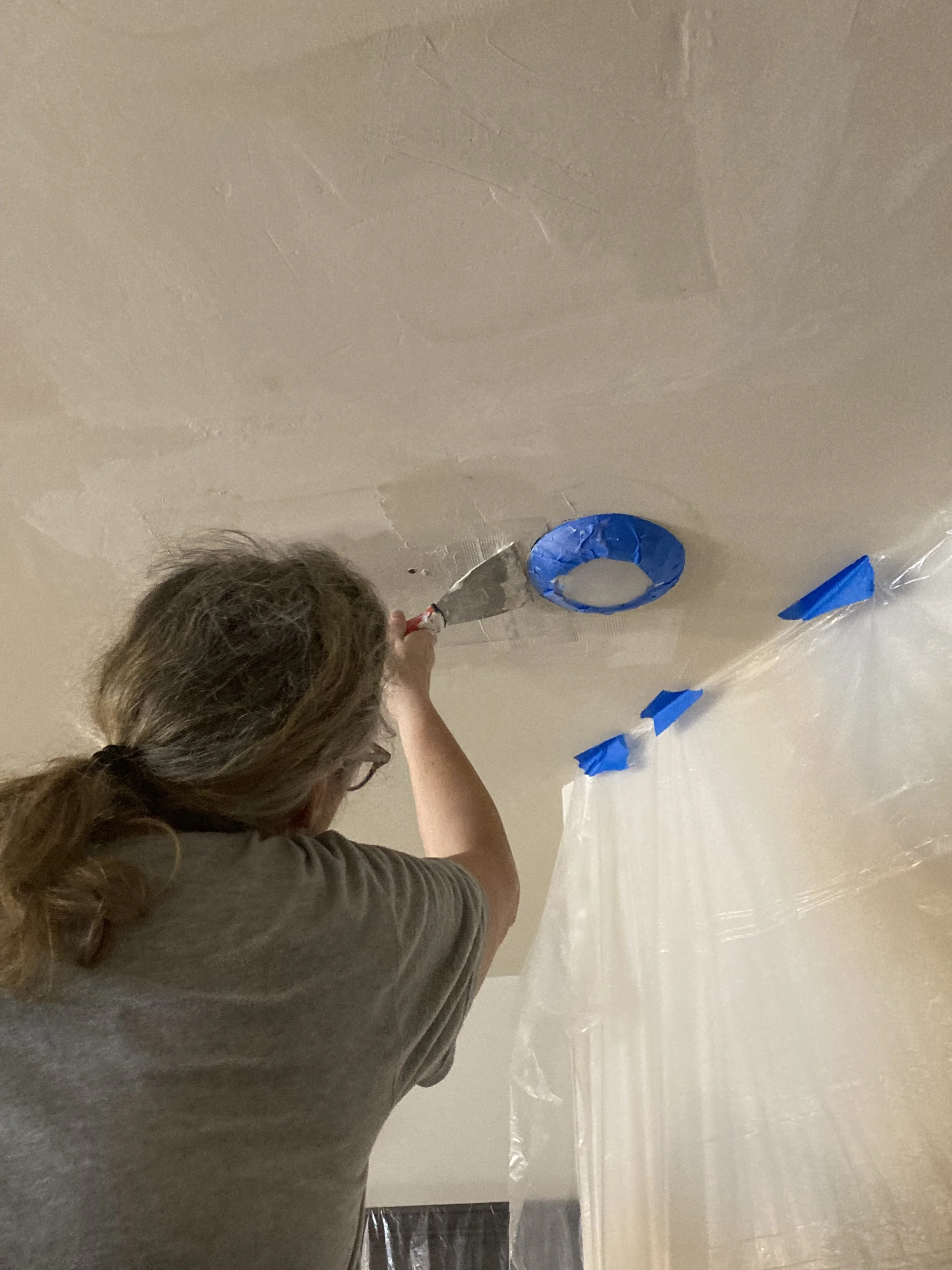 Leigh of Leigh Drywall Repair applying joint compound to a ceiling repair with a drywall knife.