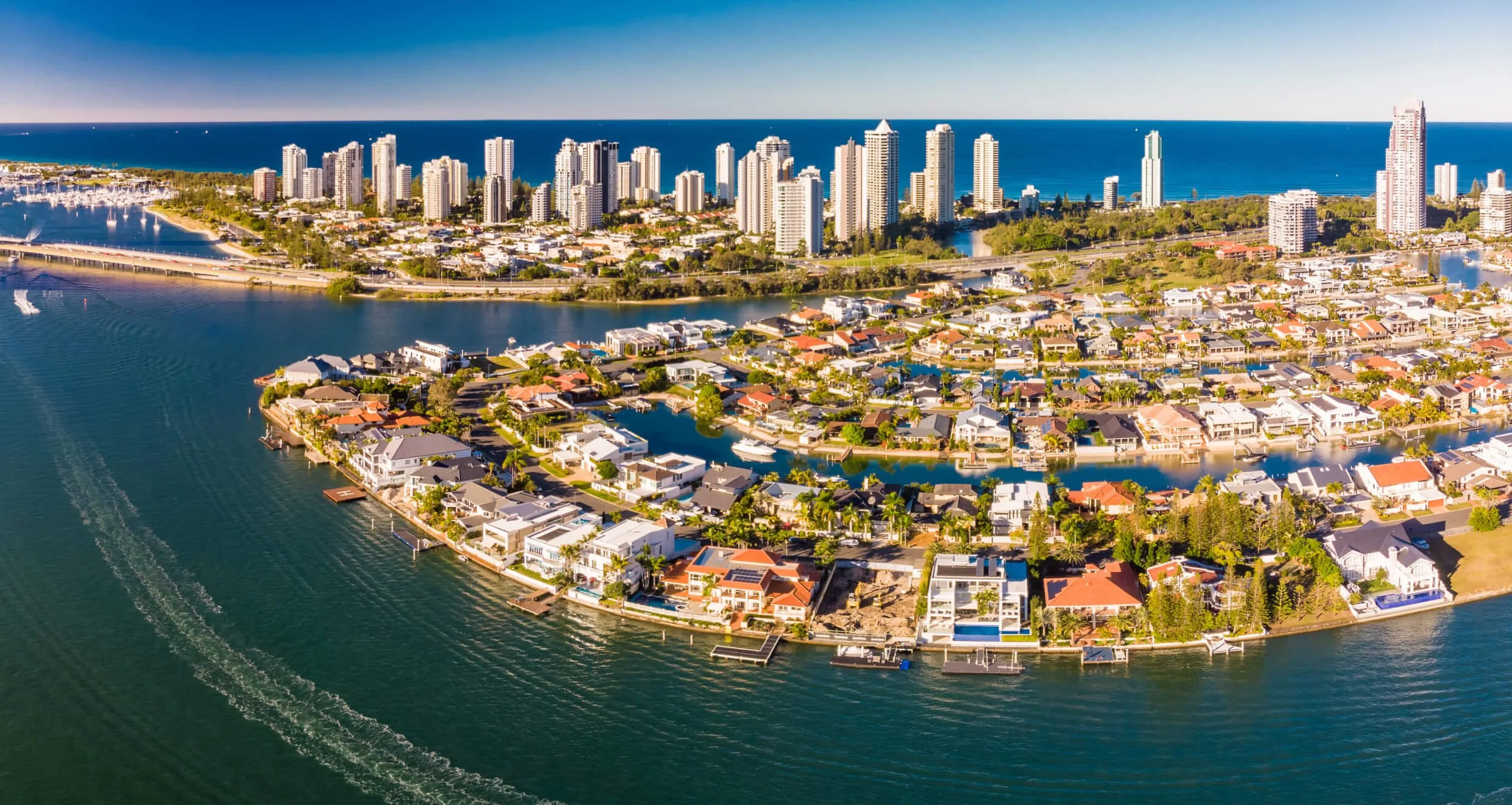 Aerial view of a coastal city with high-rise buildings, residential houses, and water canals, with the ocean in the background.