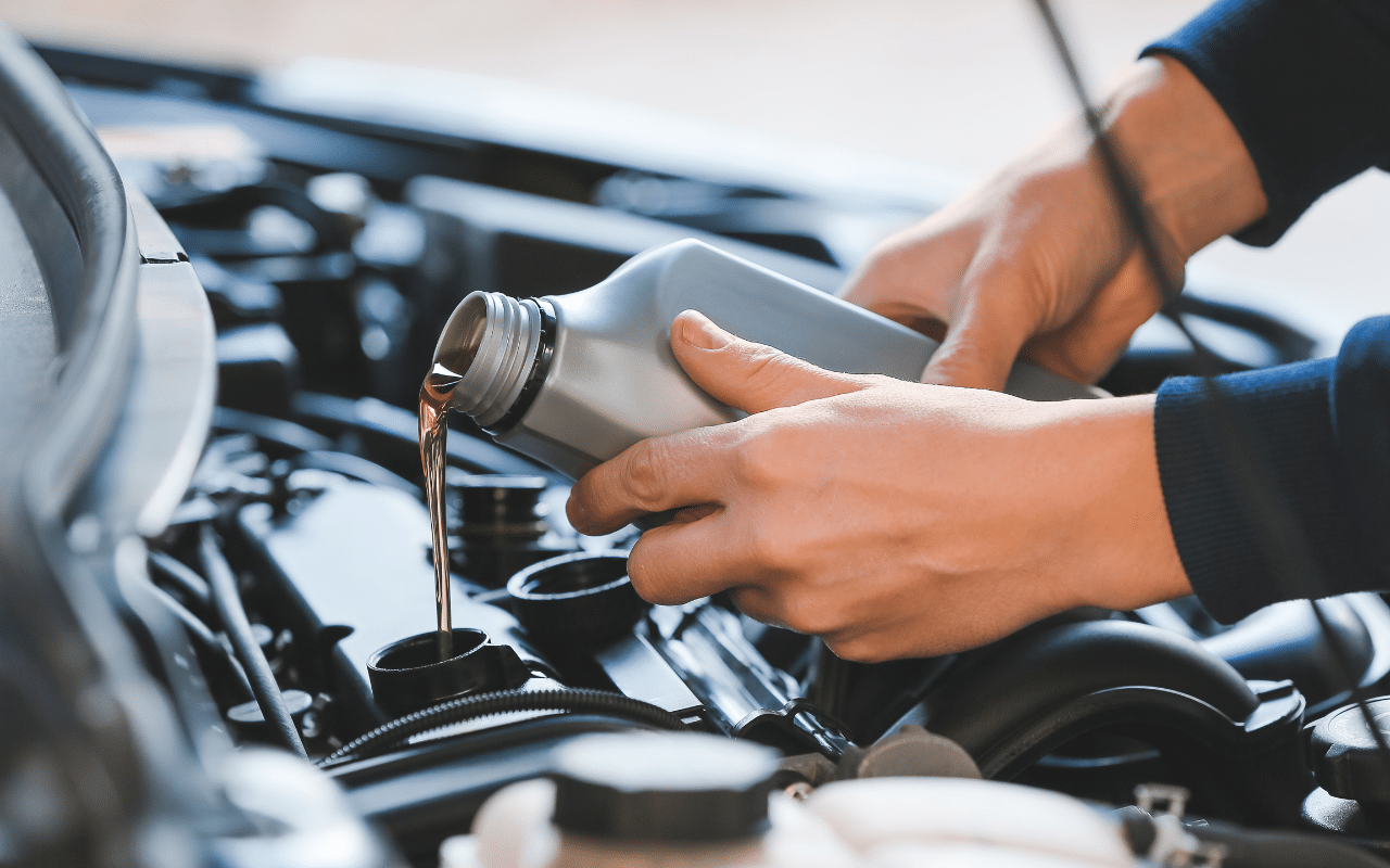 Person pouring engine oil into a car engine from a gray bottle.