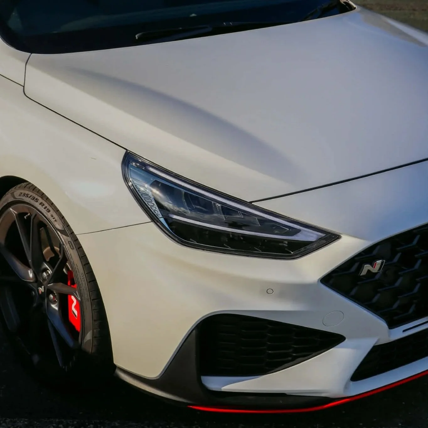 Close-up of the front of a white sports car with black grille, sleek headlight, and black wheel with red brake caliper.