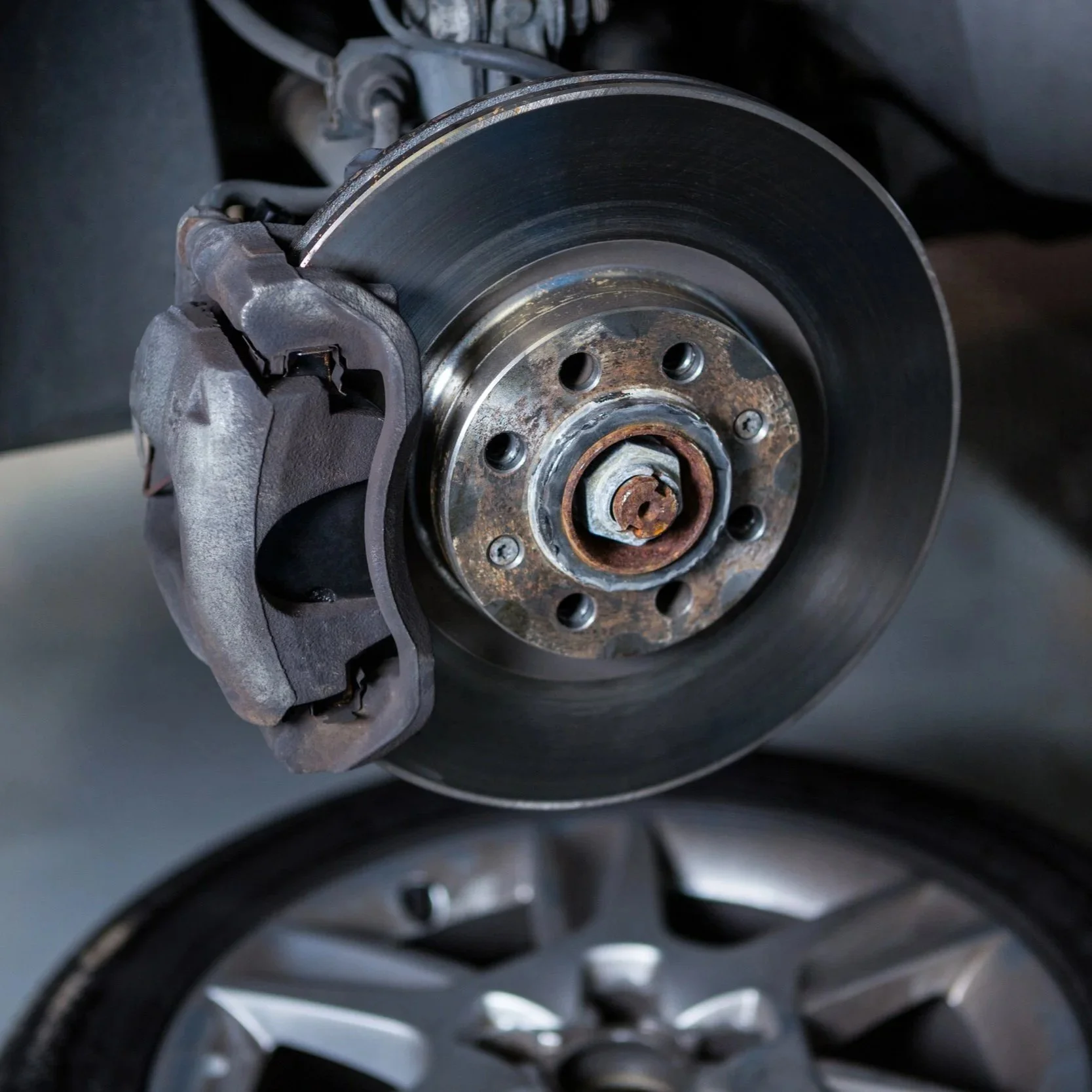 Close-up of a car's brake disc, caliper, and wheel hub, with some rust visible on parts.