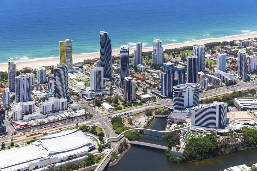 Aerial view of a city skyline with tall modern buildings along a beach, with a river running through the city, and a clear blue sky.