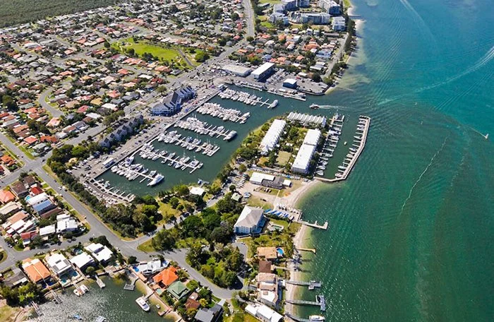 Aerial view of a marina with boats, surrounding residential neighborhood, and waterway.