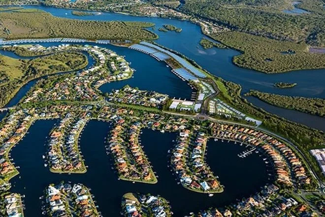 Aerial view of a residential community with houses built along winding waterways, surrounded by green forests and lakes.