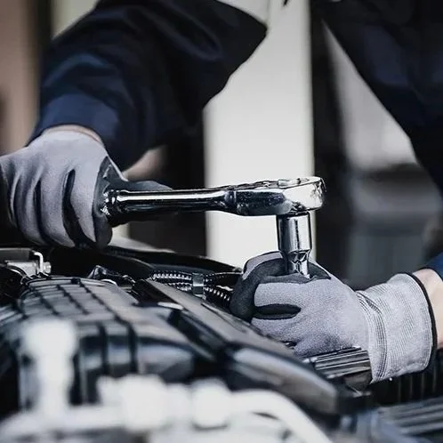 A person wearing gloves using a ratchet wrench to work on a mechanical part in a workshop.