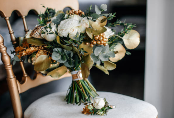 A bouquet of white and gold flowers with green leaves and gold accents placed on a light-colored cushioned chair.