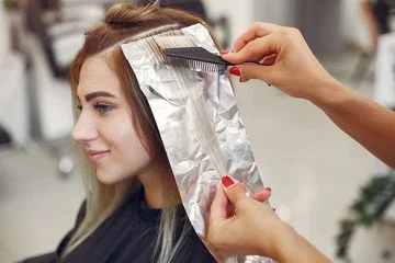 Stylist applying hair color with foil highlights to a client’s blonde hair at a salon.