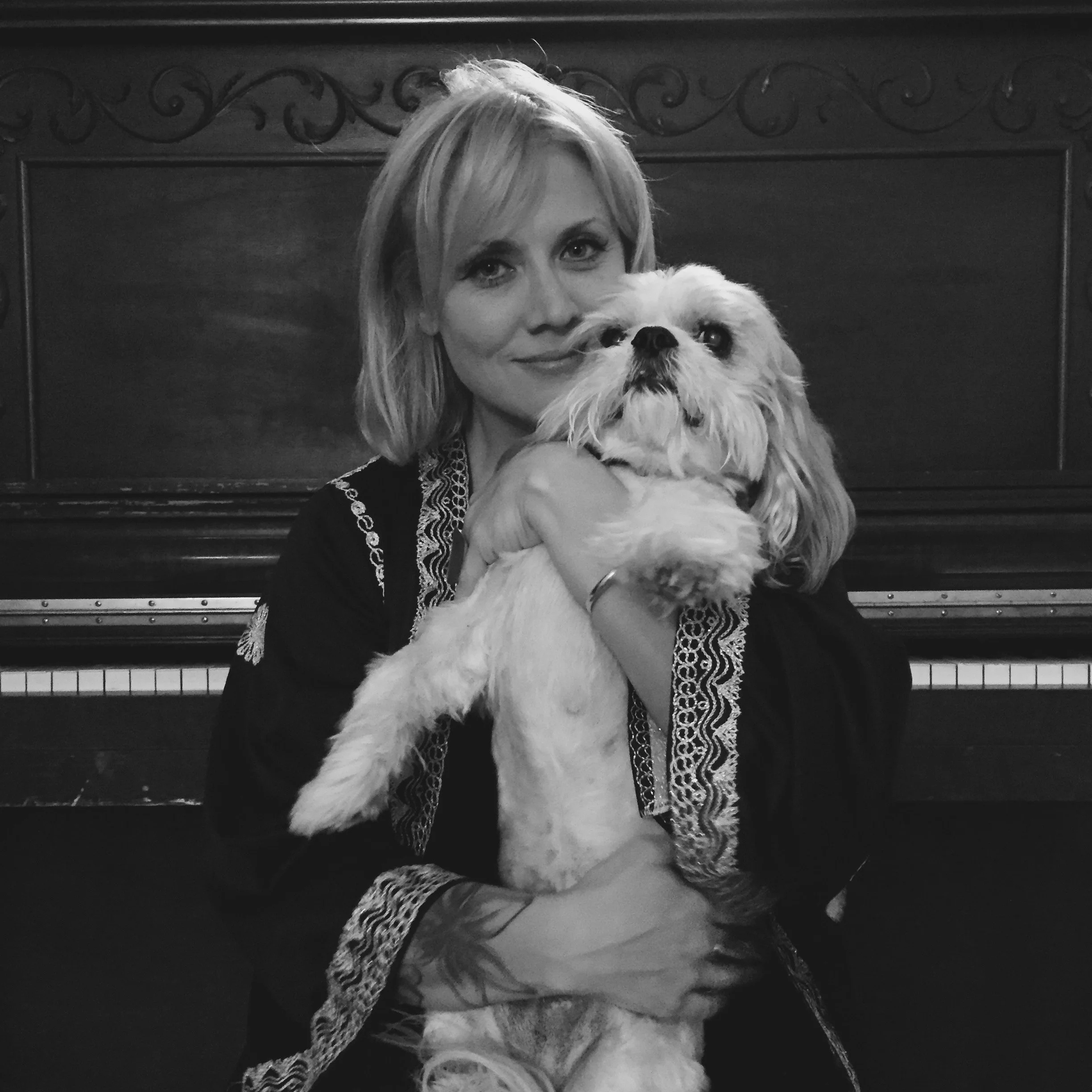 A woman holding a small dog in front of a piano.