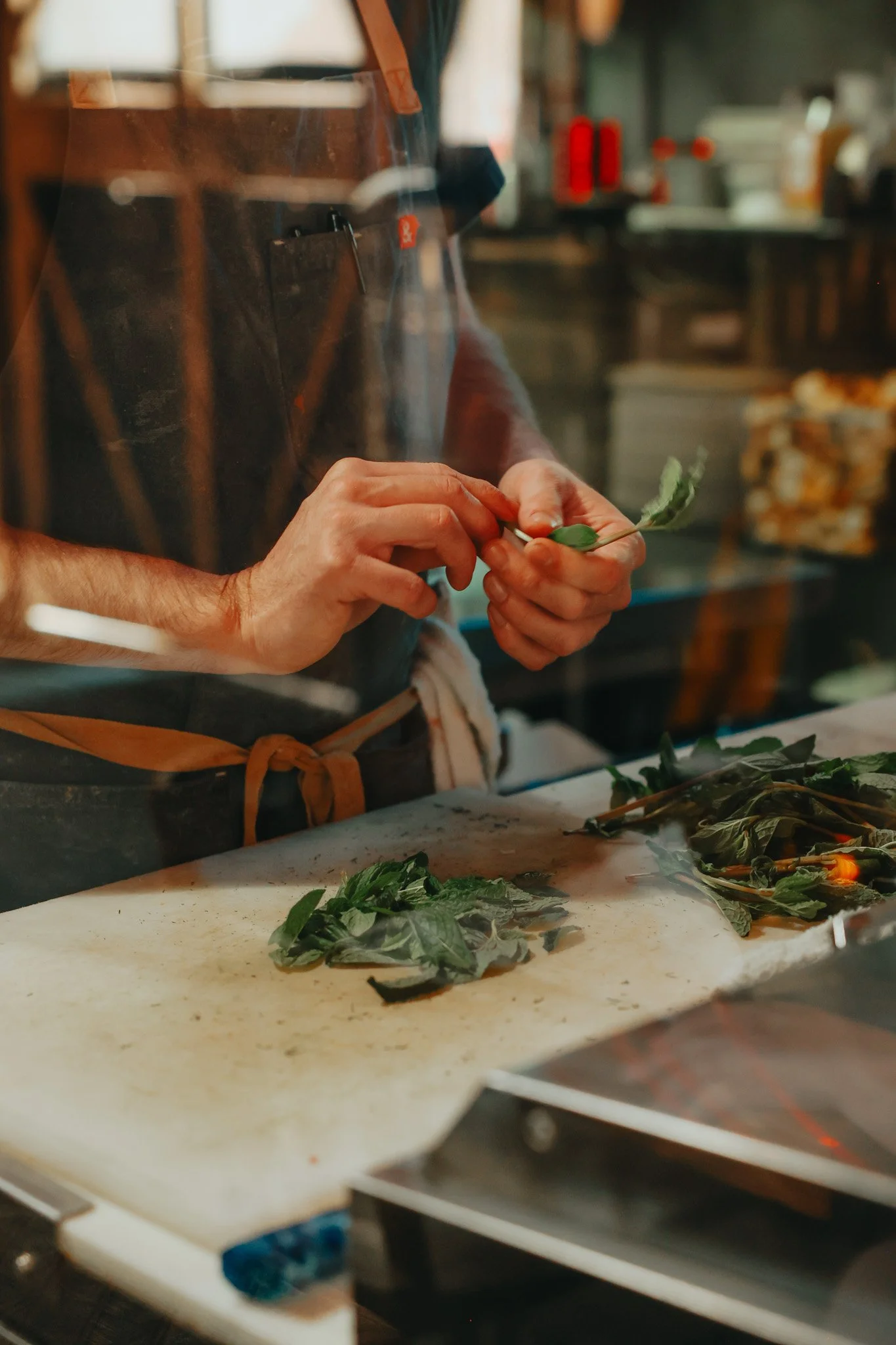 A person preparing fresh herbs, possibly basil, on a kitchen counter with a cutting board, in a professional kitchen environment.