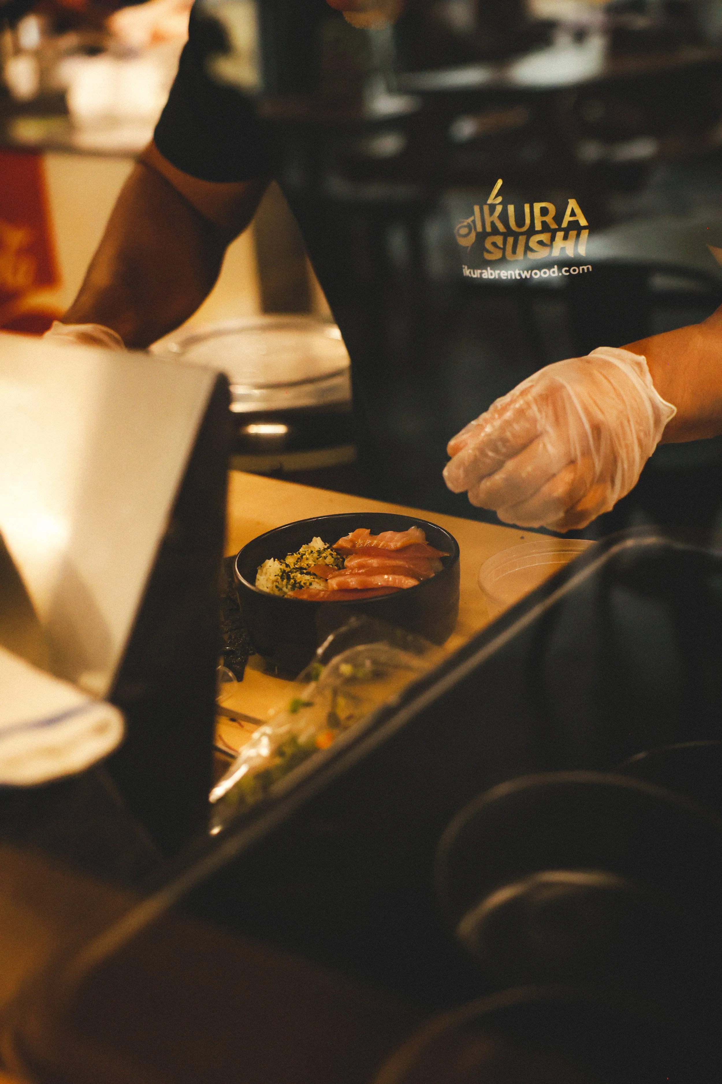 A sushi chef wearing gloves prepares sushi at a counter in a restaurant.