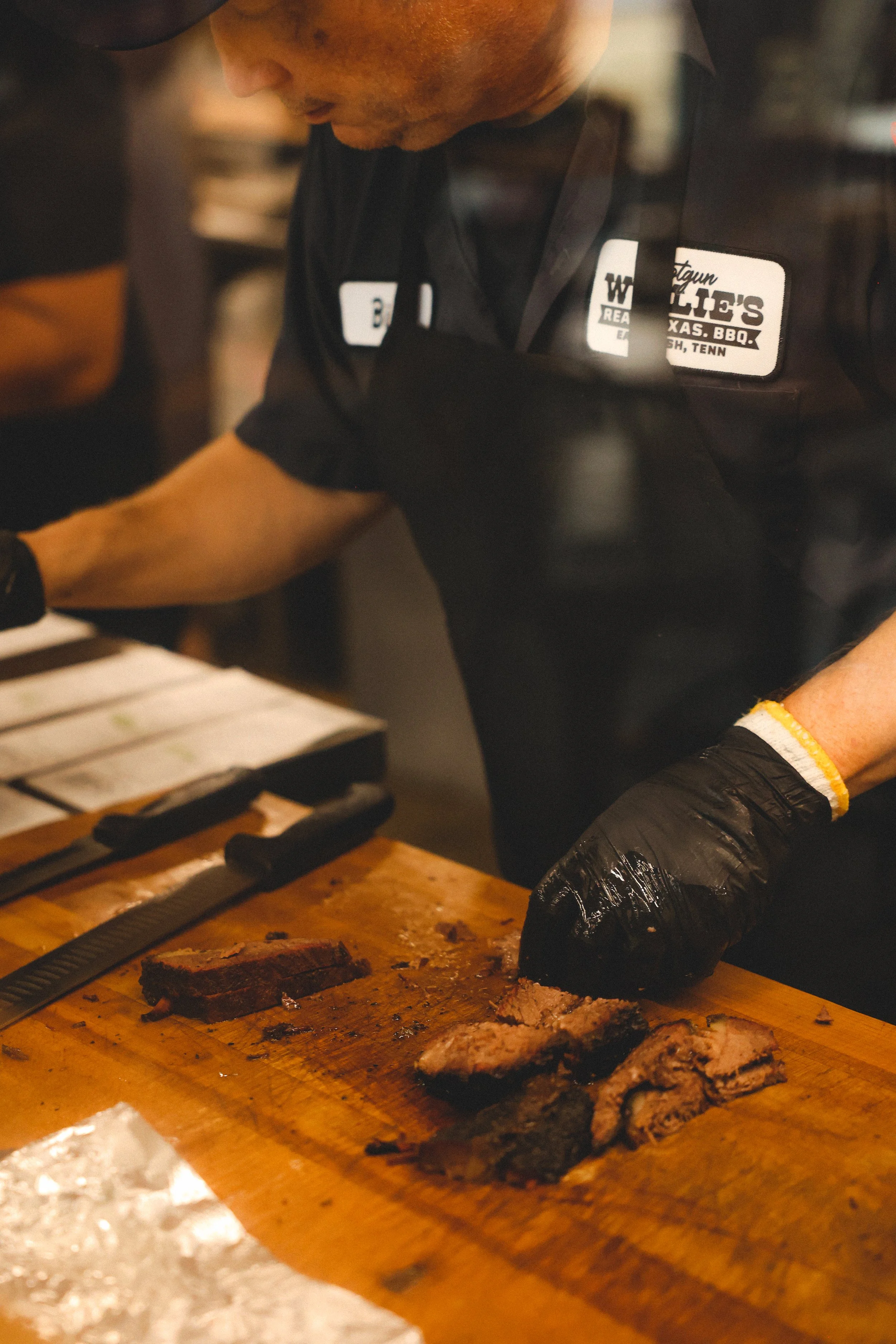 Close-up of a man slicing cooked beef brisket on a wooden cutting board in a barbecue restaurant.