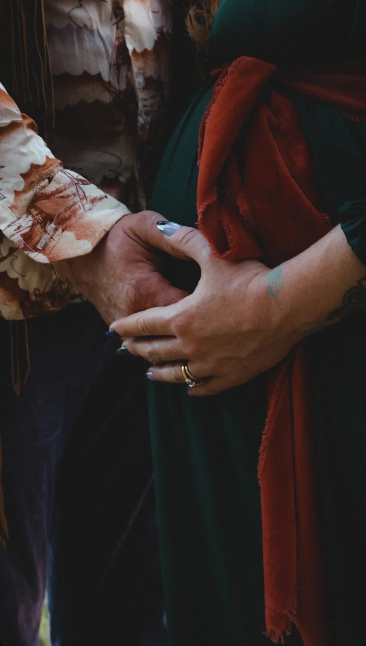 Two people holding hands, one with a tattoo and rings, the other with colorful painted nails.