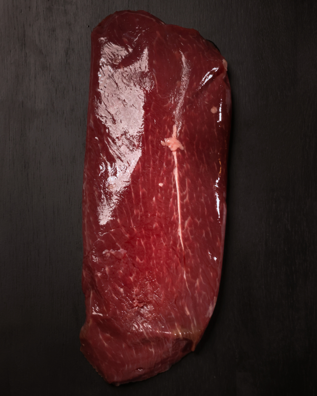 A large cut of raw red meat on a dark surface.