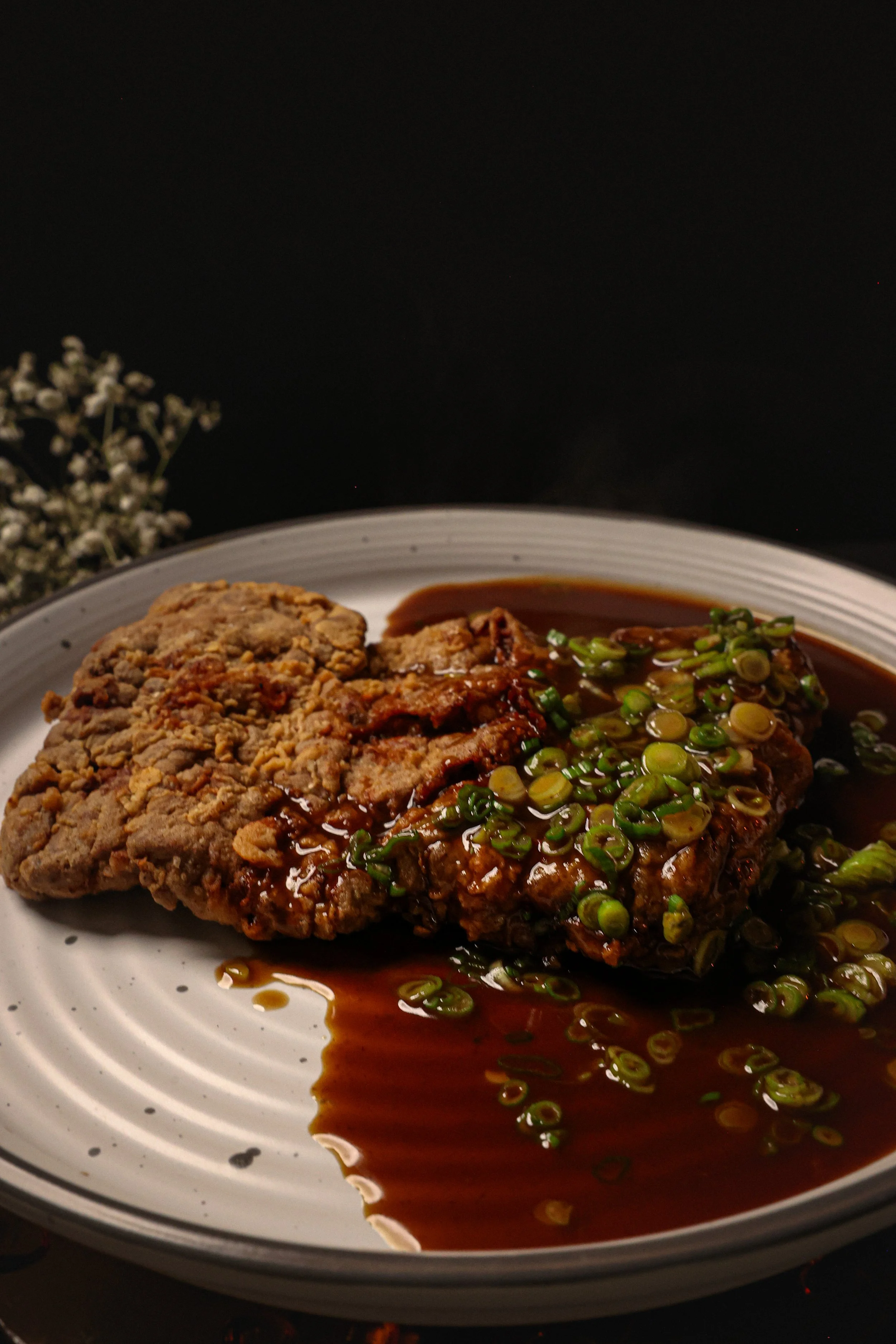 Fried chicken and meatloaf with green onions and sauce on a white plate.
