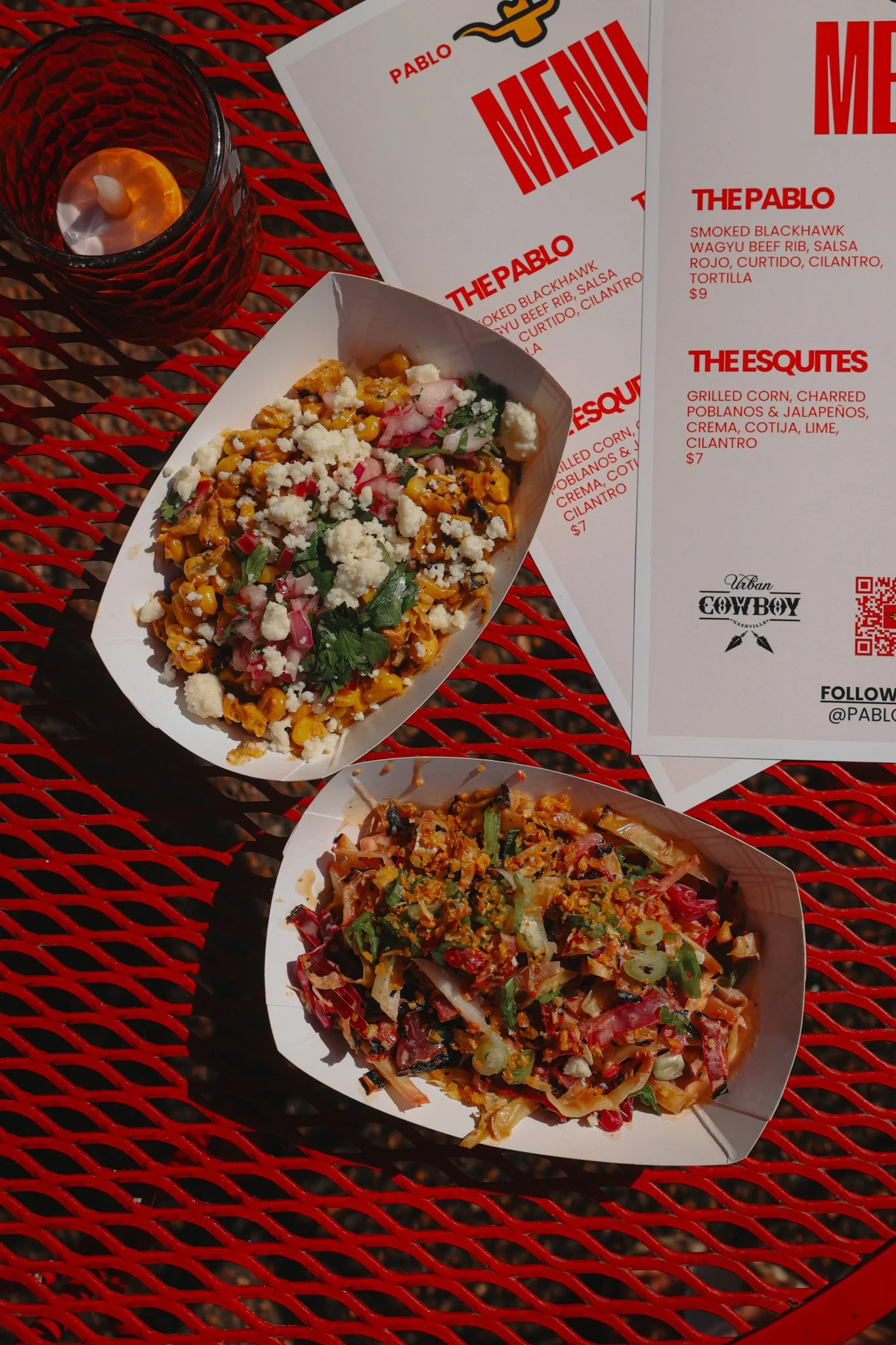 Two bowls of salad and a candle on a red metal table, with menu papers from Pablo restaurant.