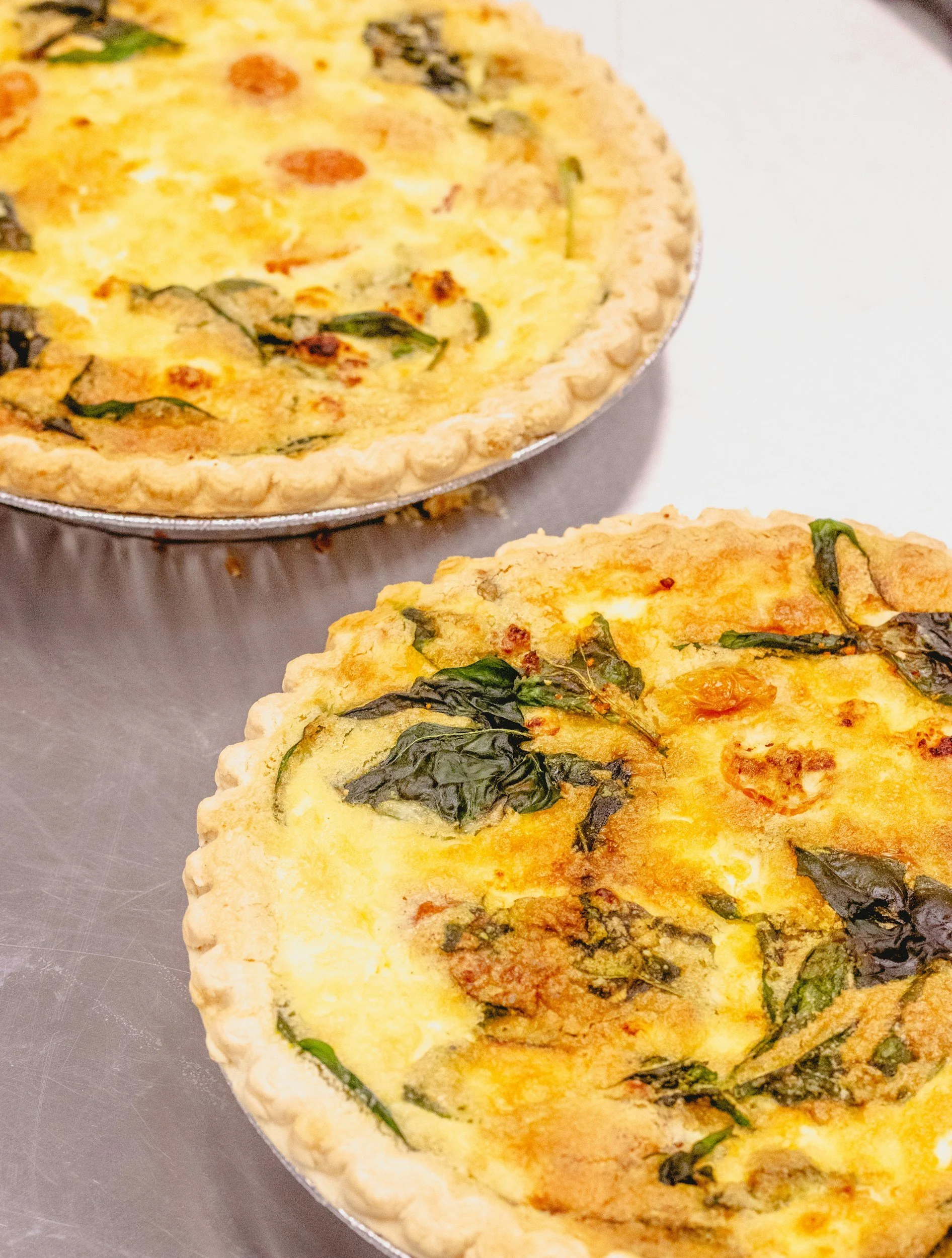 Two cooked spinach and cheese quiches on a metal surface.