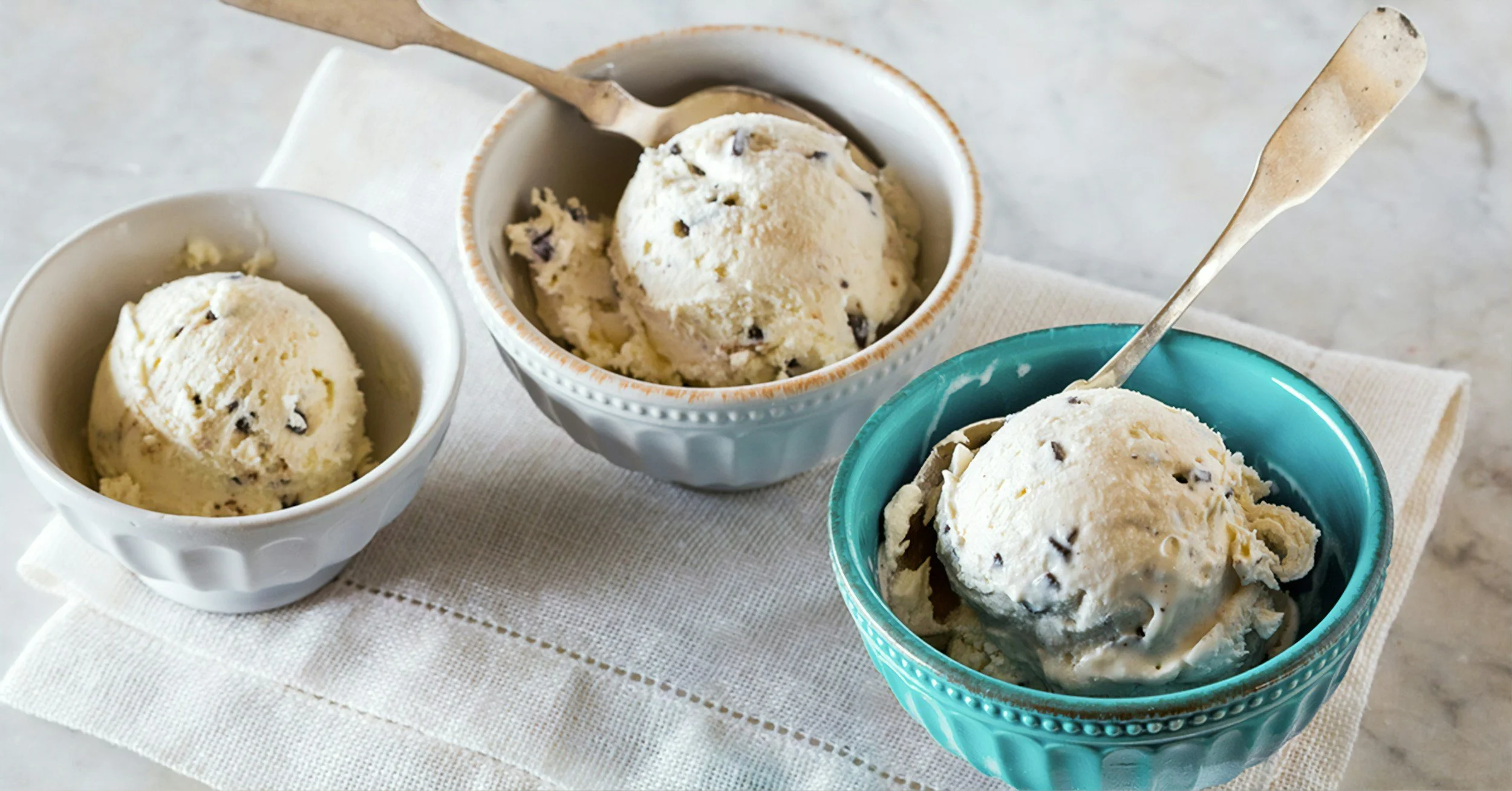 Three bowls of vanilla ice cream with chocolate chips on a kitchen towel.