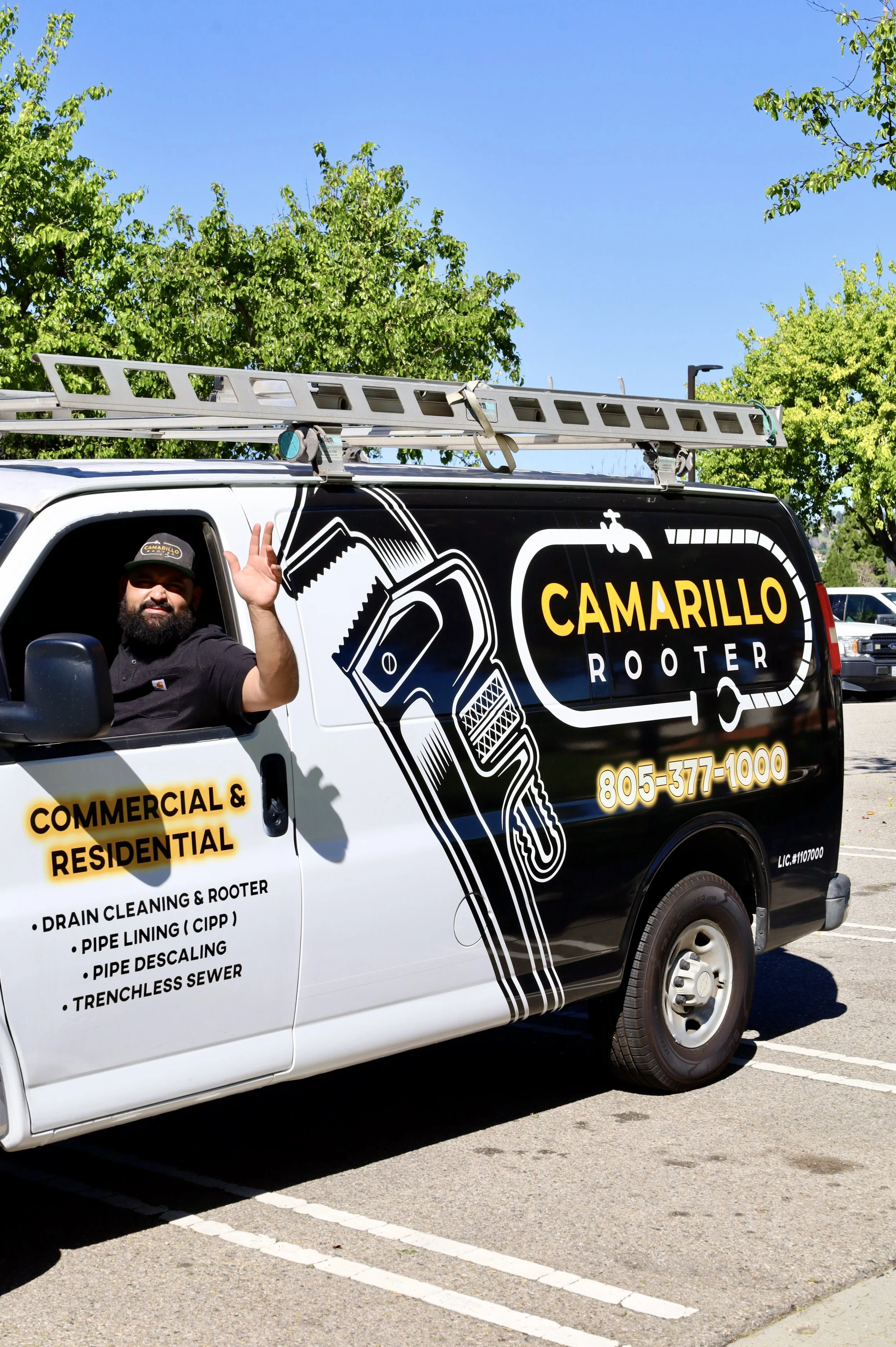 Lonnie Jimenez, the owner of Camarillo Rooter, is leaning out the driver side window of the Camarillo Rooter van with a friendly wave.