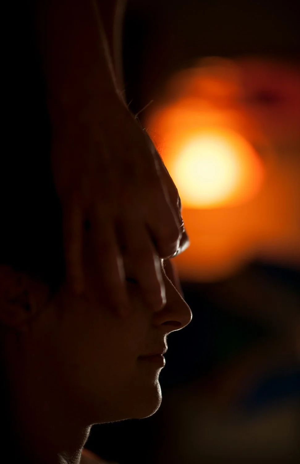 Silhouette of a woman with closed eyes against a bright orange sunset background.
