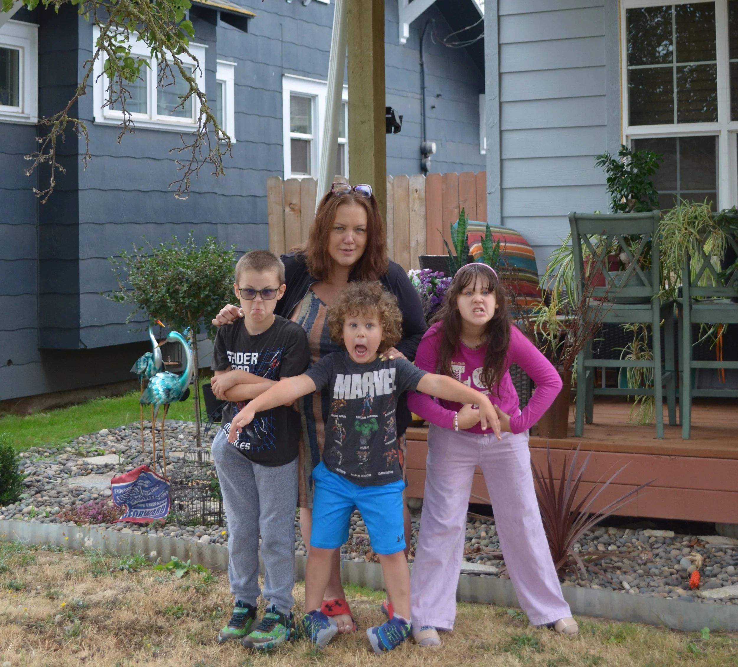 A woman and three children standing together outside in a yard, making funny faces and posing.