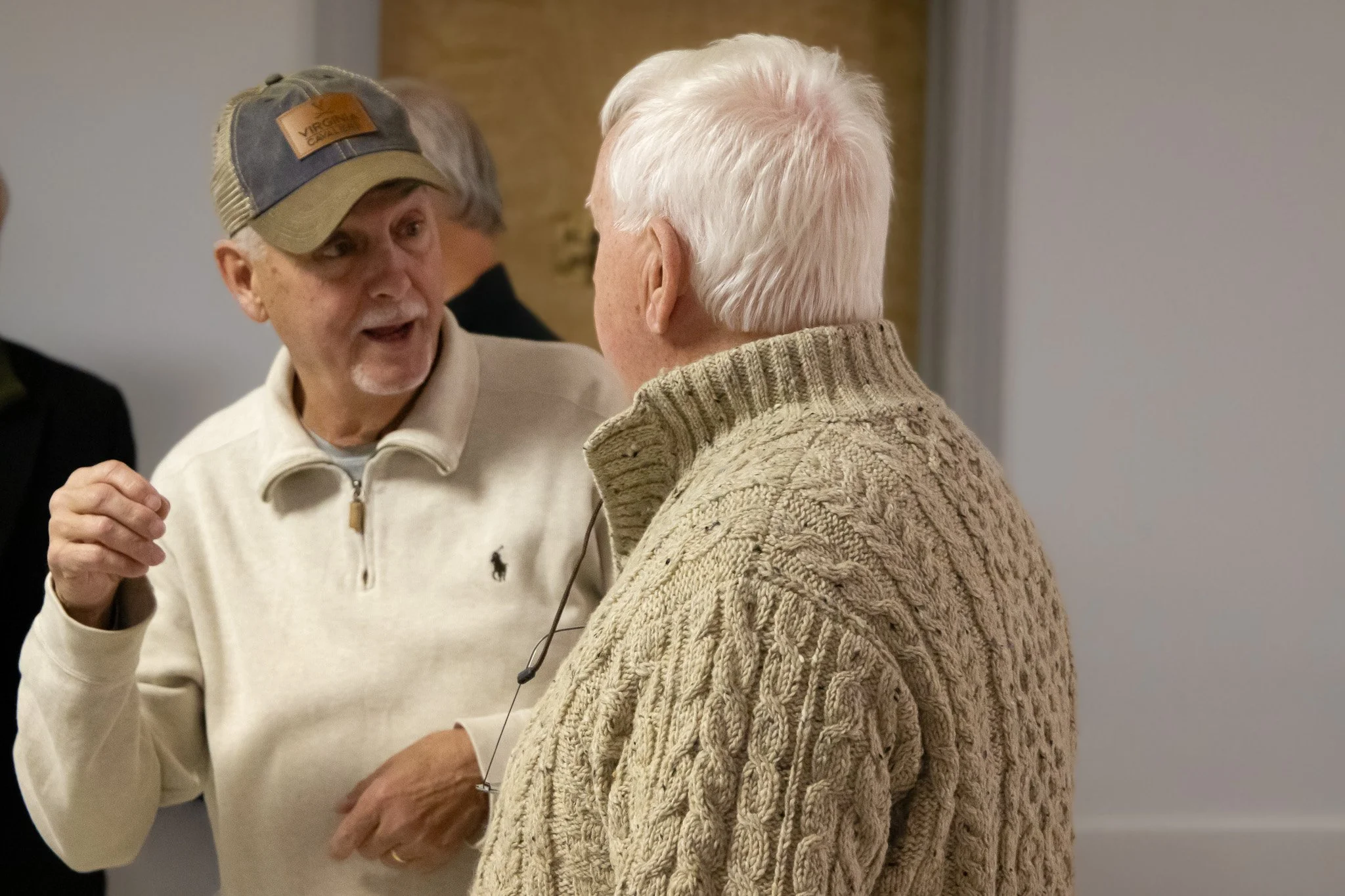 Two elderly women engaged in conversation, one wearing a cream sweater, the other in a knitted beige cardigan.