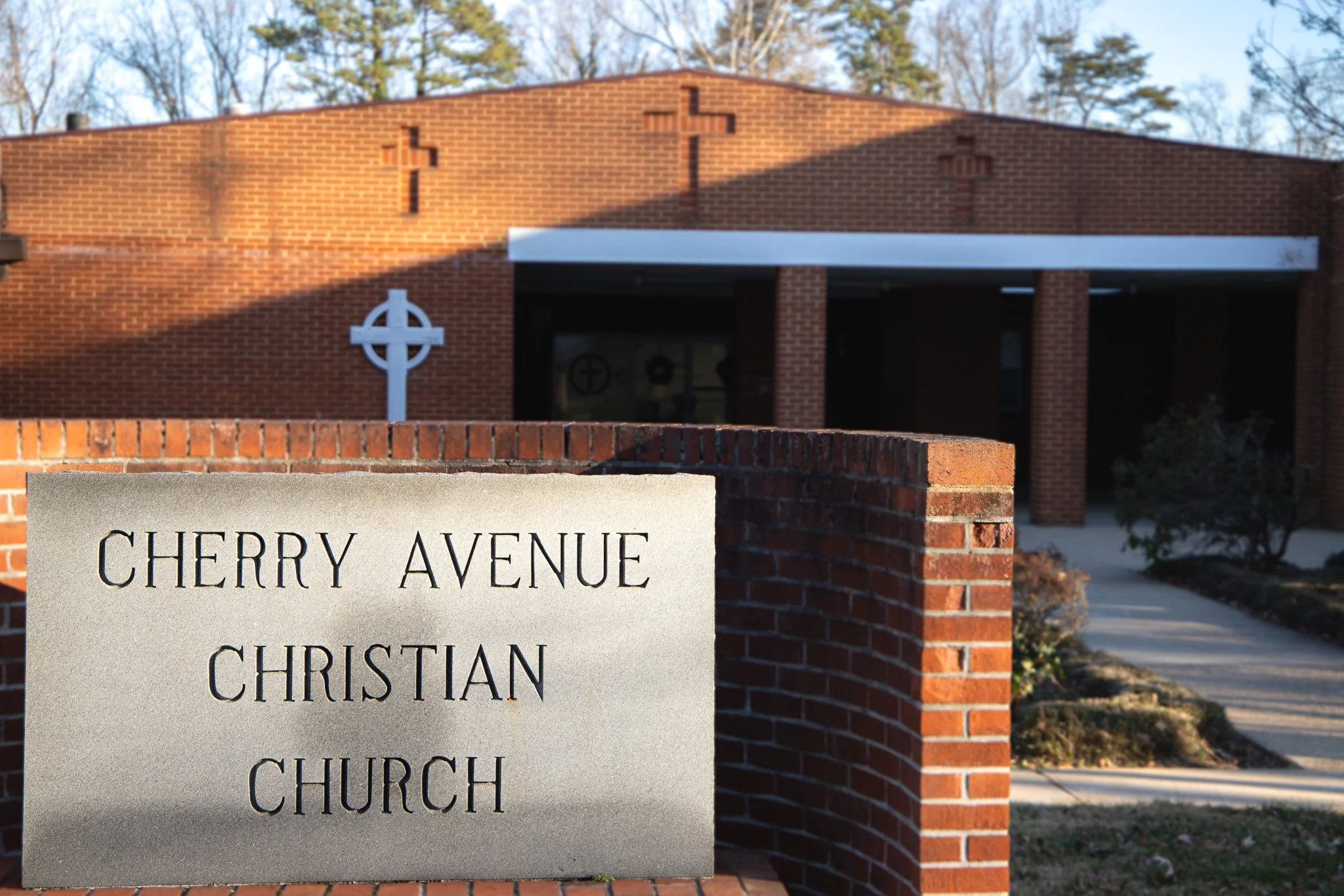 Street sign reading Cherry Avenue Christian Church in front of a brick church building with crosses and a white awning.
